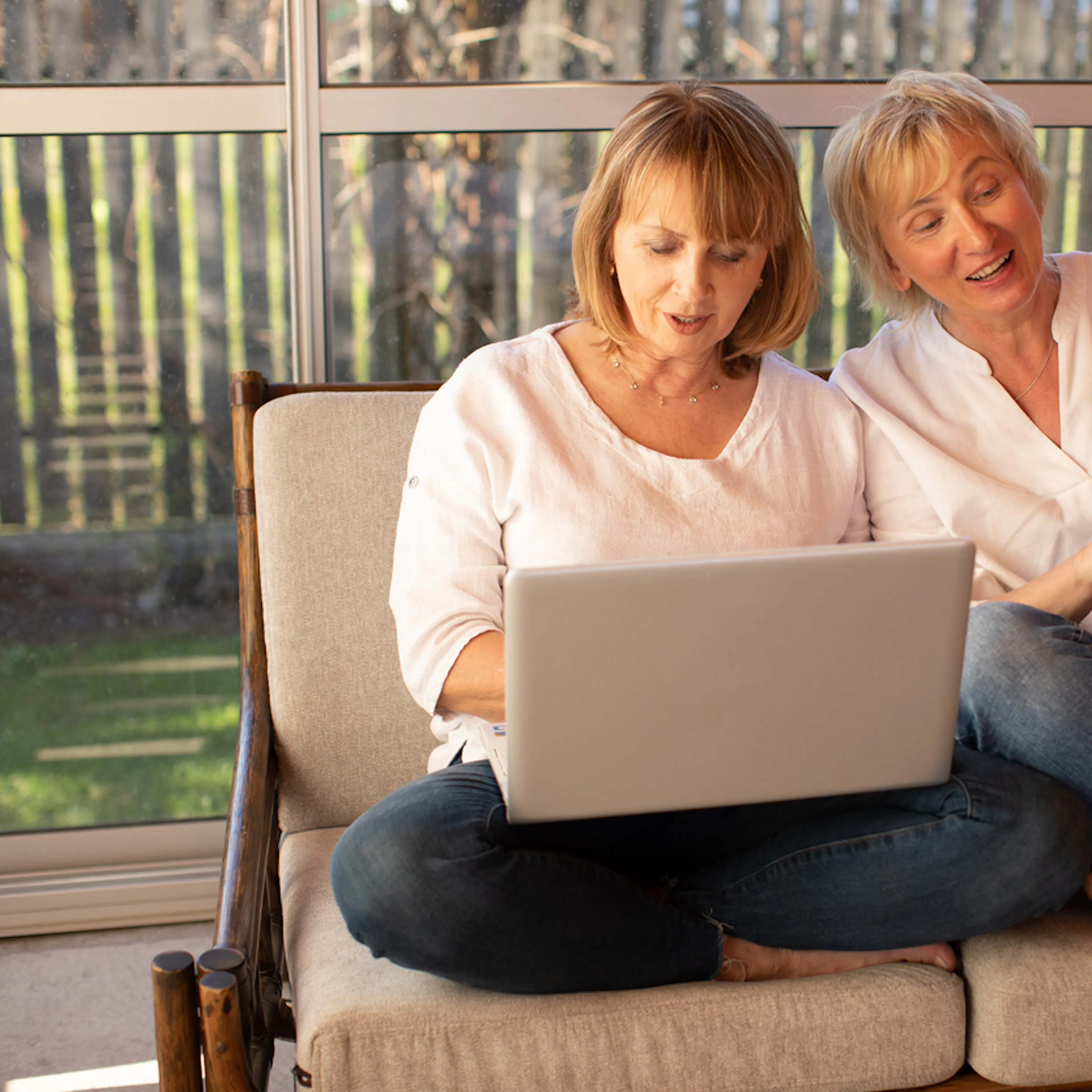 two women middle aged sitting on sofa with laptop wearing jeans