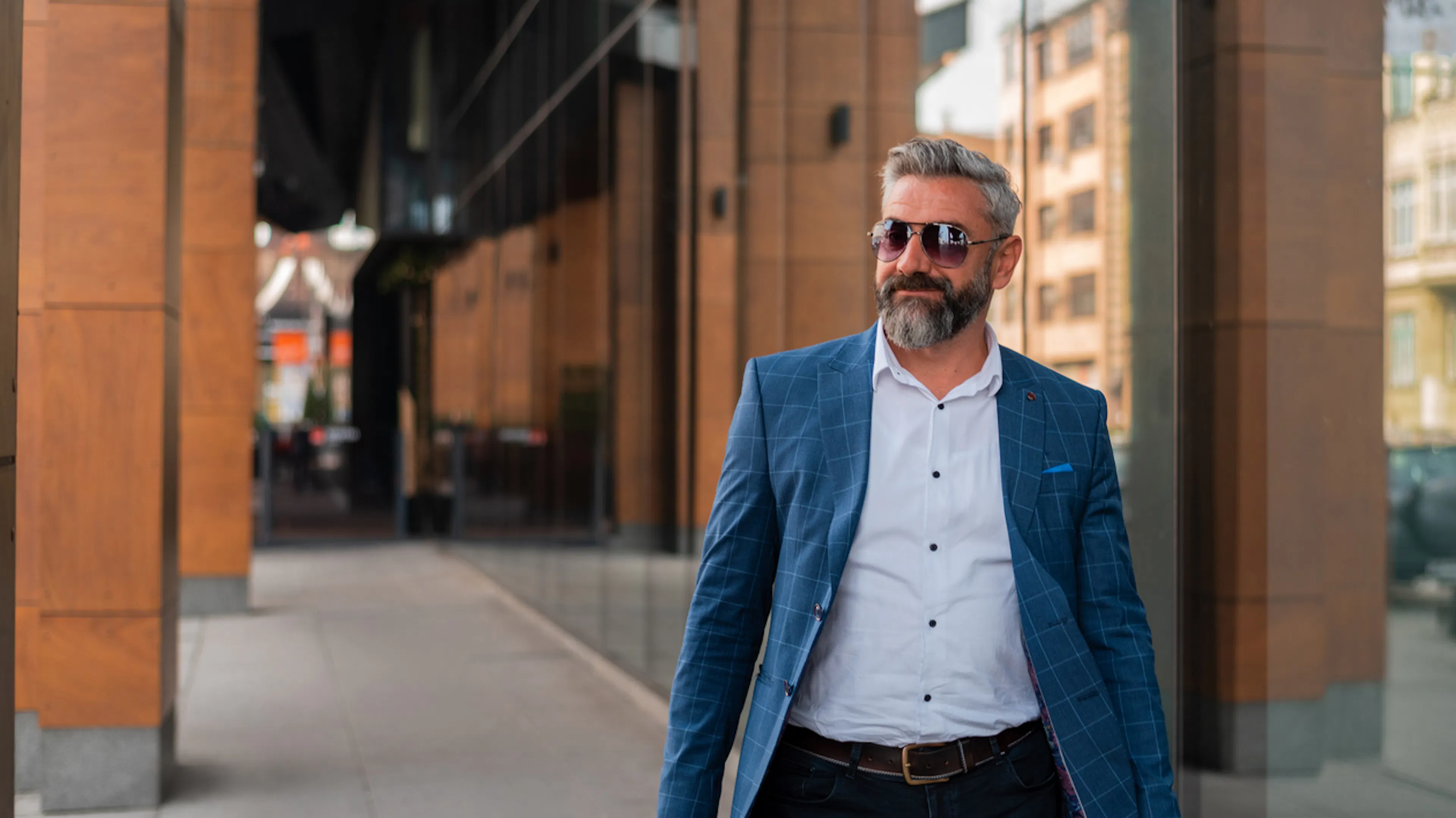 Middle aged man in blue jacket and sunglasses walking past an office