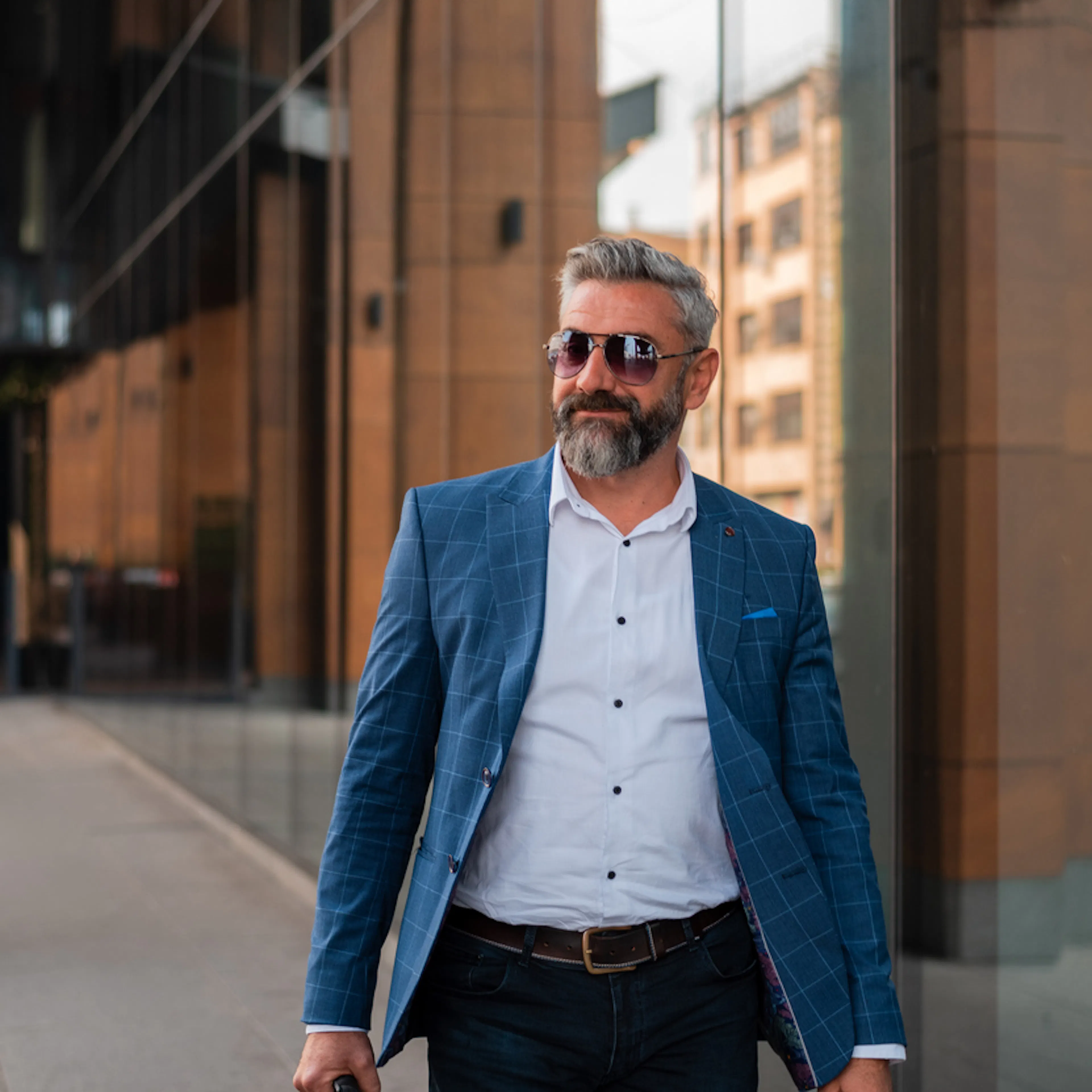 Middle aged man in blue jacket and sunglasses walking past an office