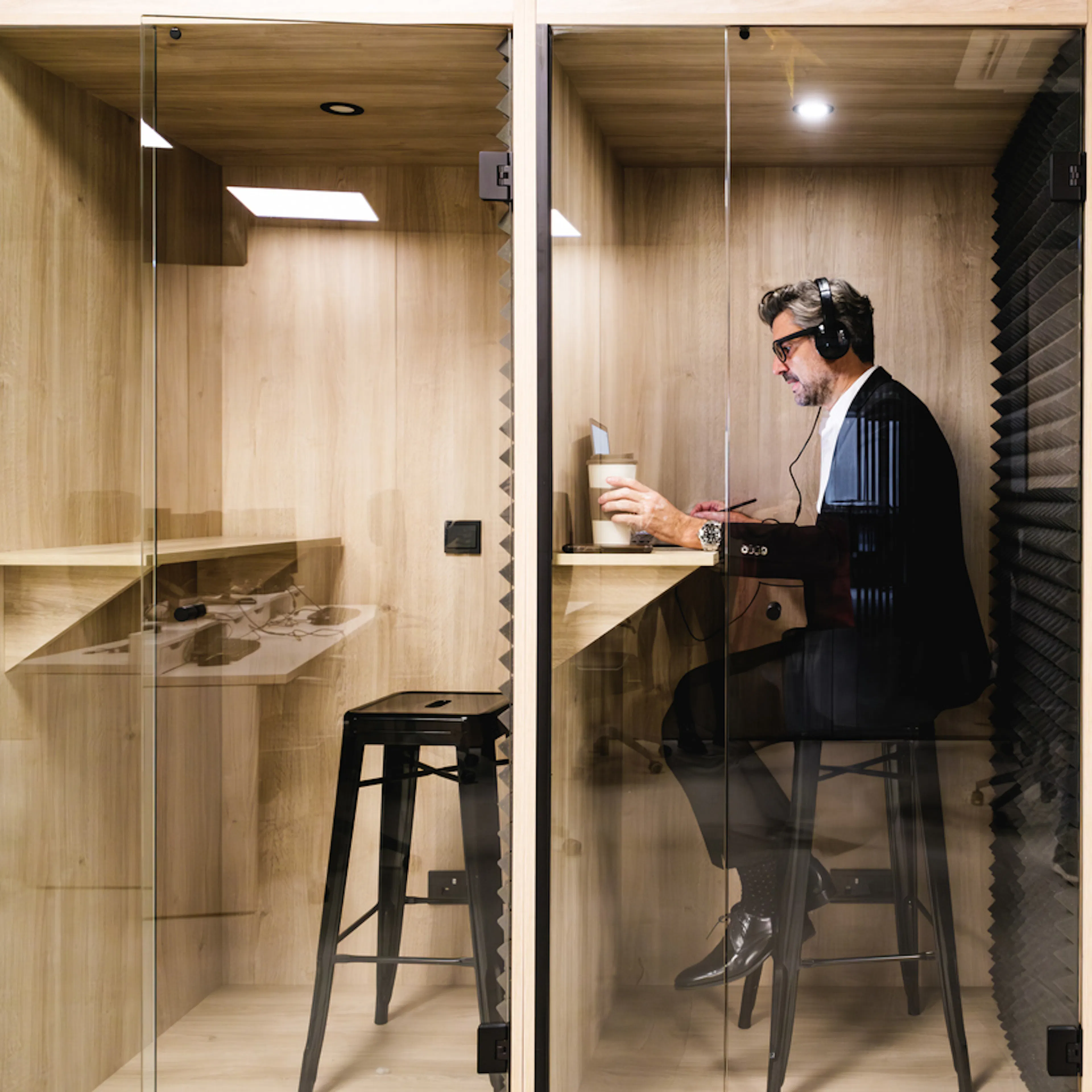 Man in suit sitting on a stool at a desk pod in an office