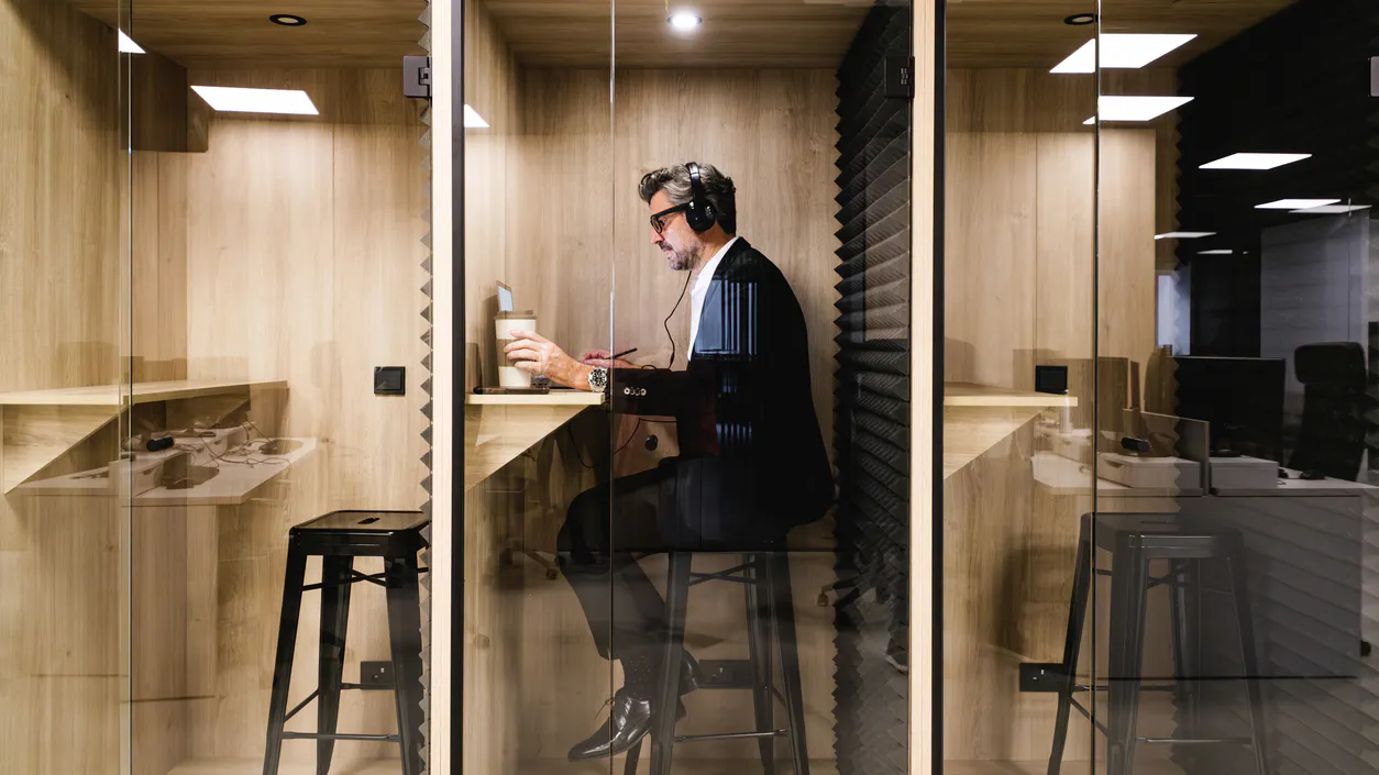 Man in suit sitting on a stool at a desk pod in an office