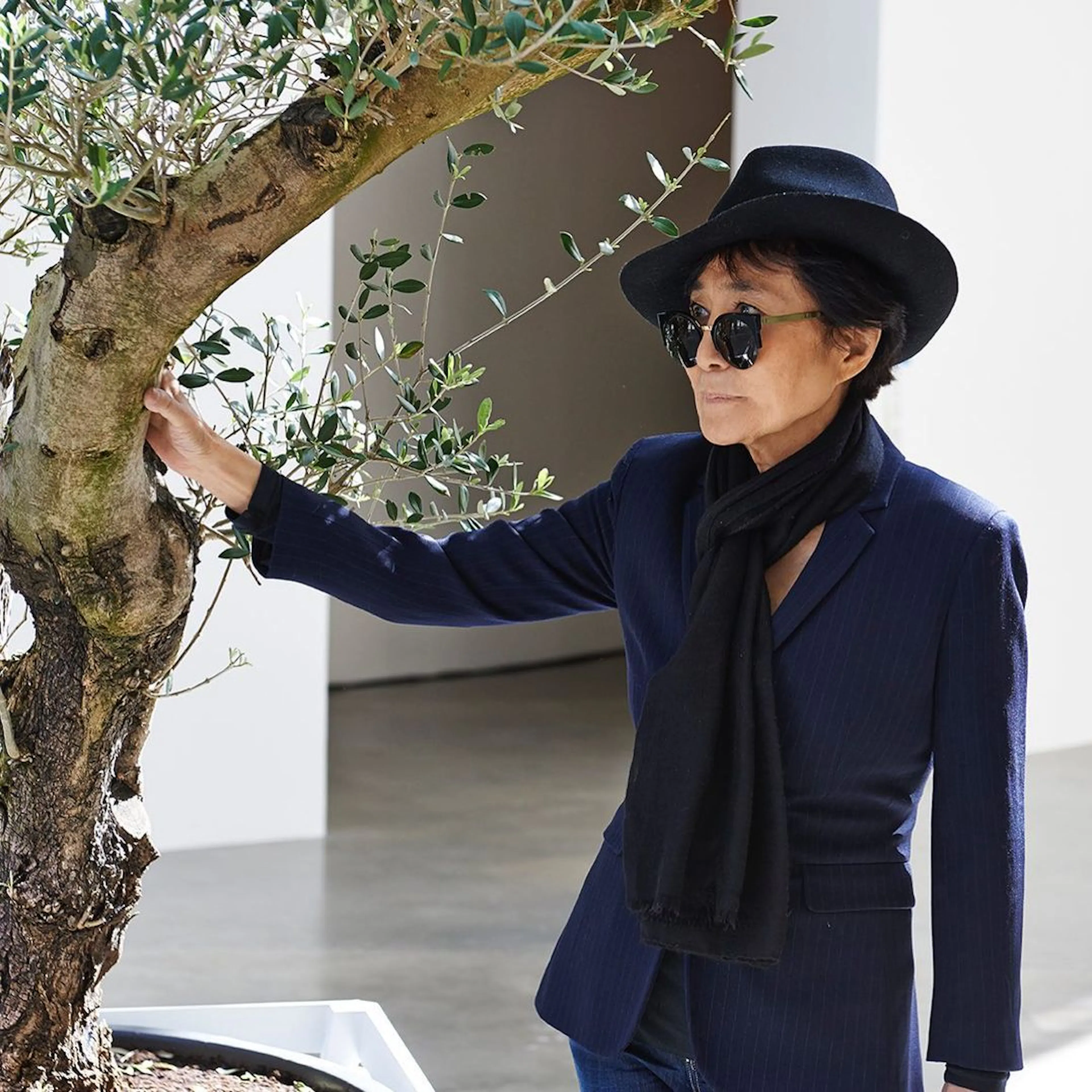 Yoko Ono poses next to a tree in her trademark hat