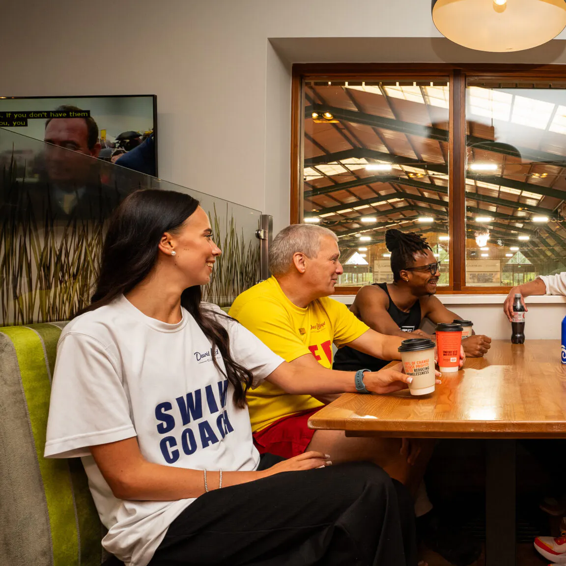Group of employees from David Lloyd Leisure sitting around a table chatting and drinking coffee.