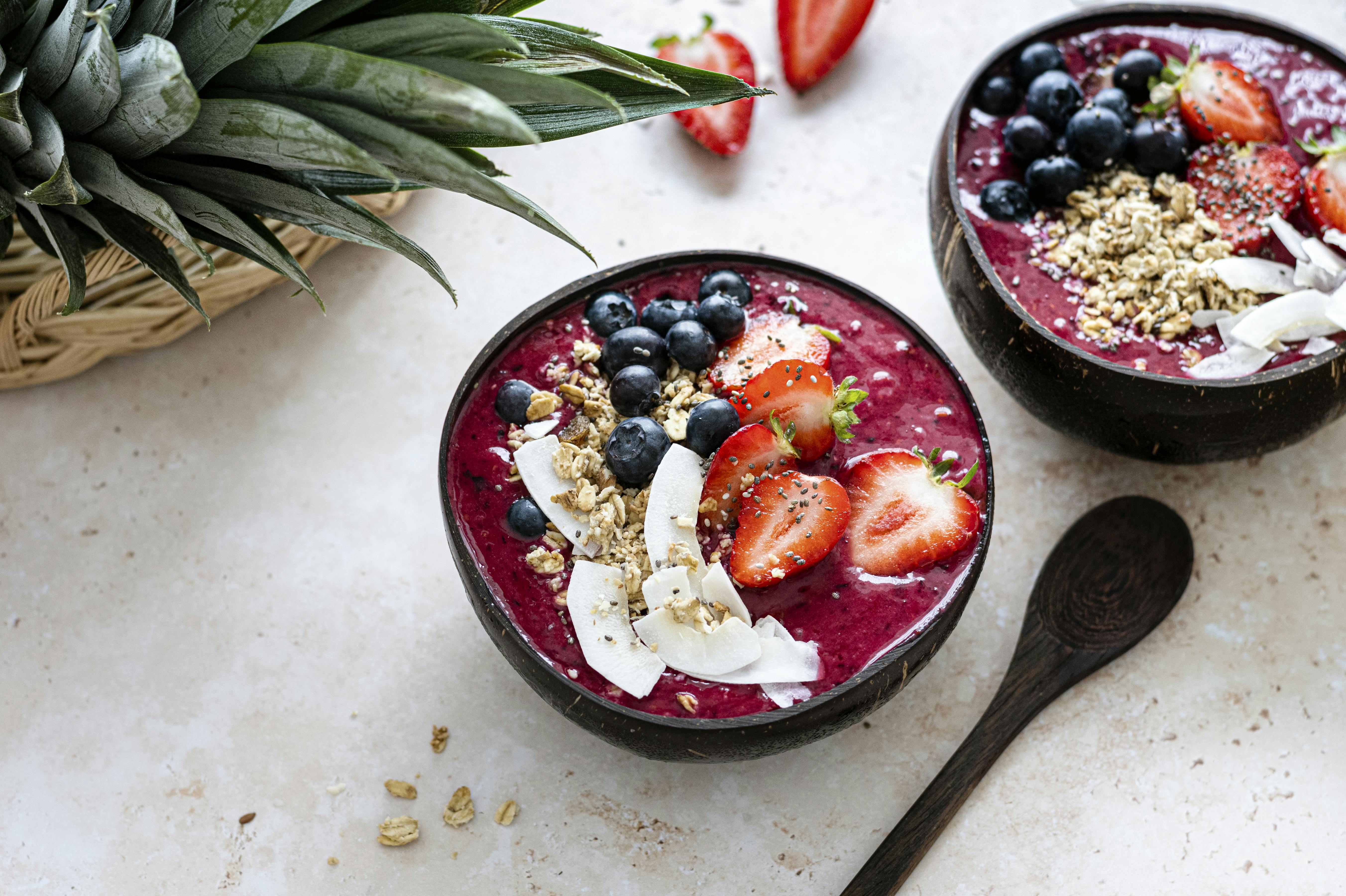 A picture of two acai bowls topped with blueberries, coconut, strawberries, and granola.