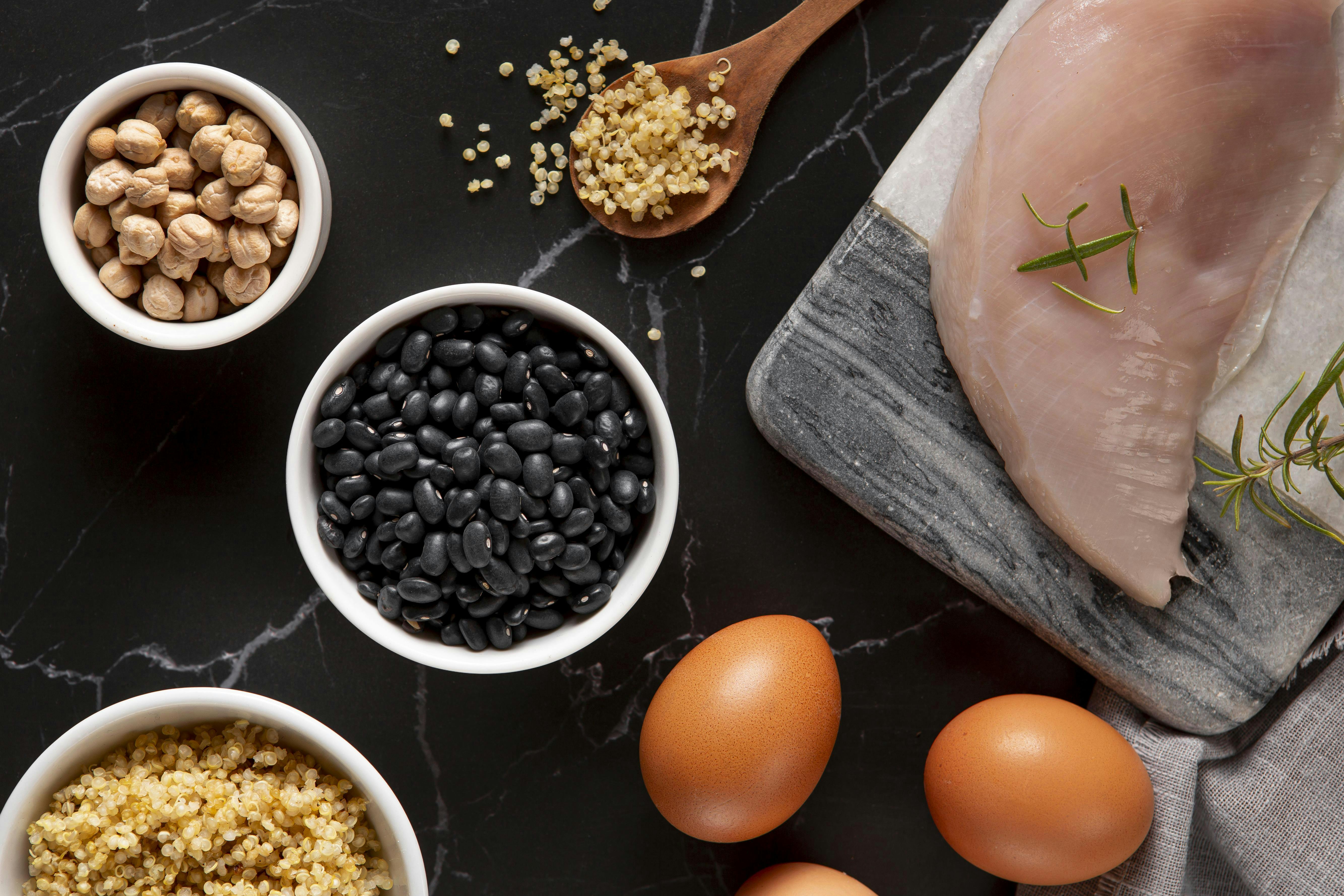 picture of uncooked chicken breast, eggs, black beans, and quinoa.