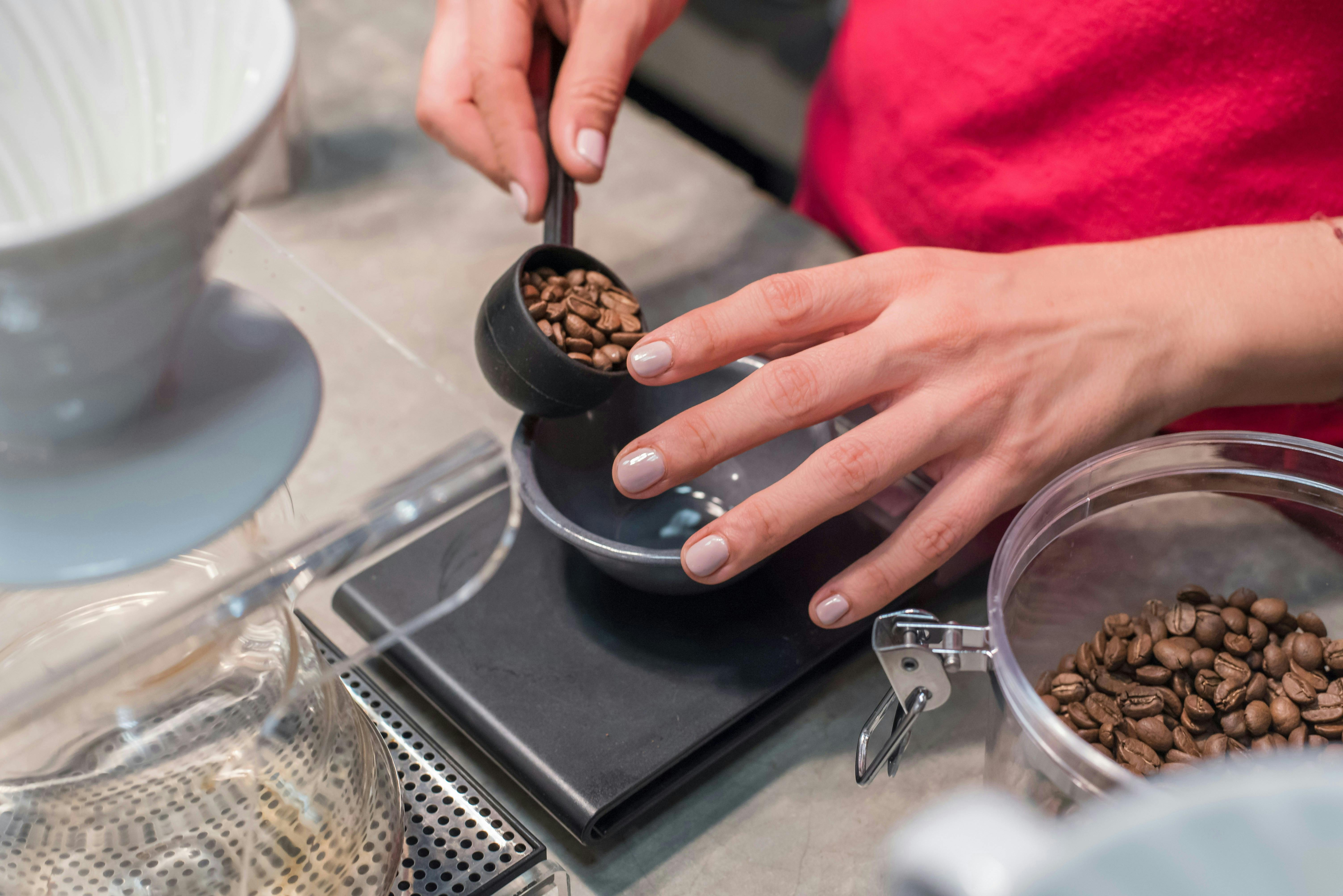 A person is scooping and measuring coffee beans with a food scale.