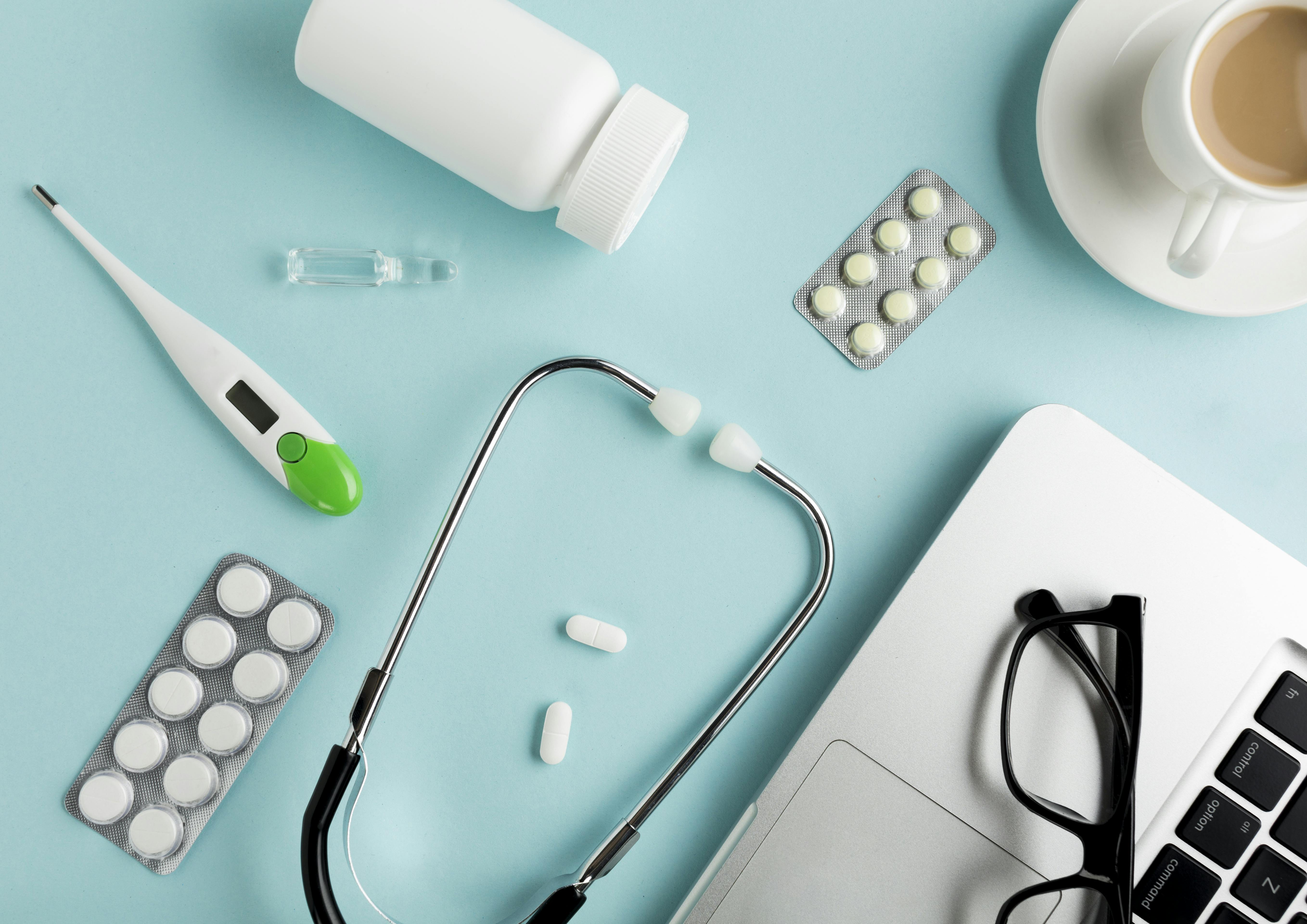 Picture of pills, stethoscope, a cup of coffee, glasses, and a laptop.