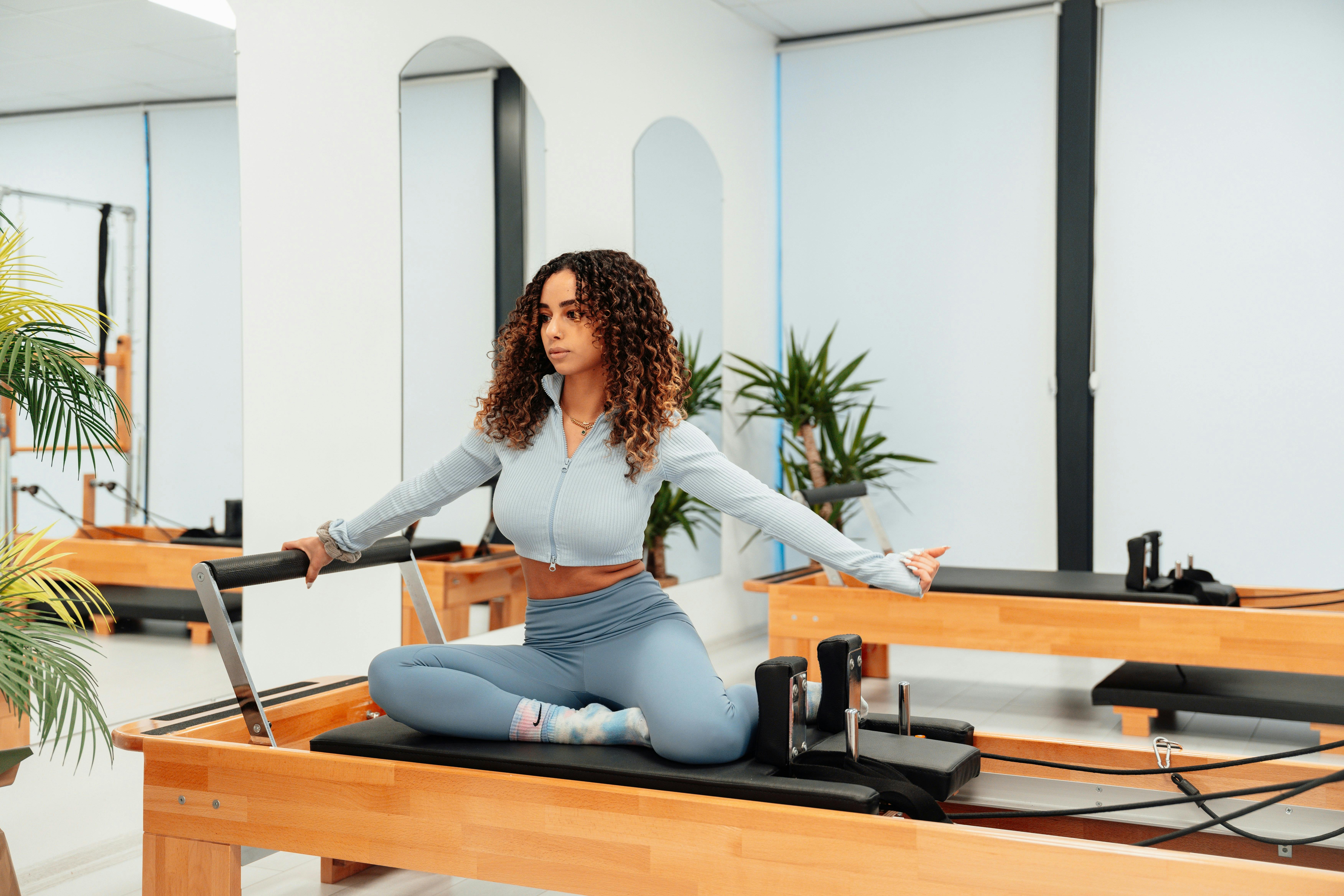 The same woman is on the reformer machine in a seated position.