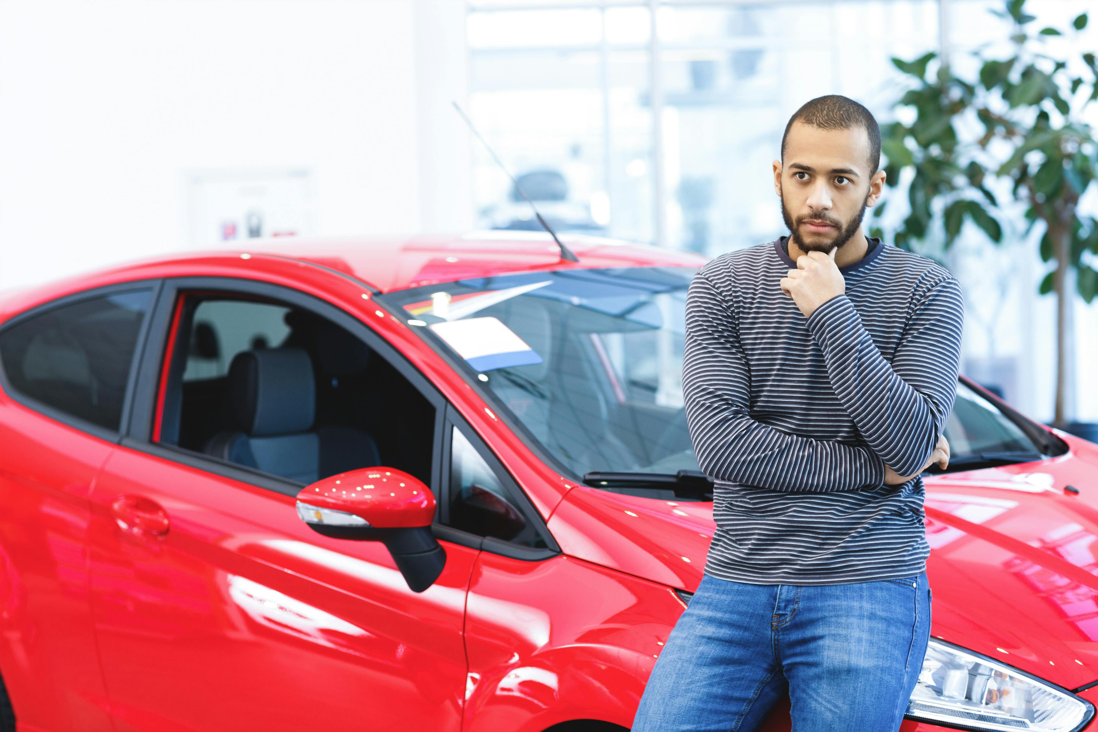 african american man contemplating while leaning against a red car