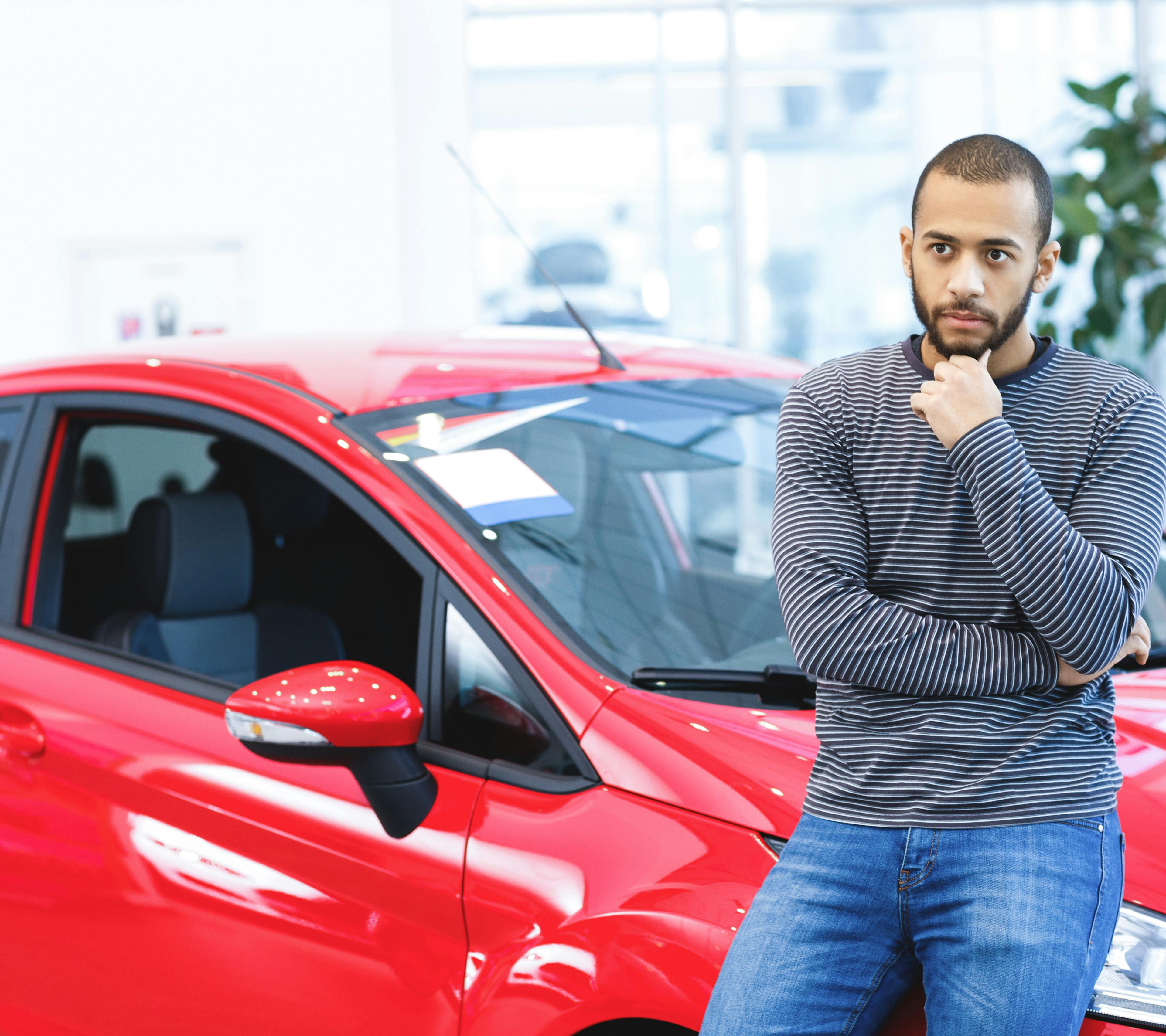 african american man contemplating while leaning against a red car