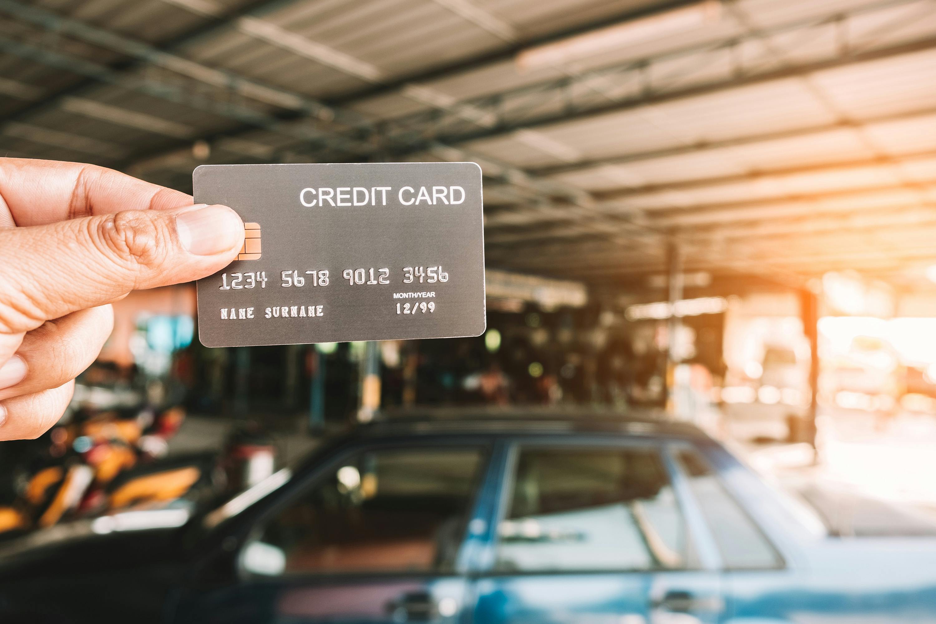 a person holding a credit card with a car in the background