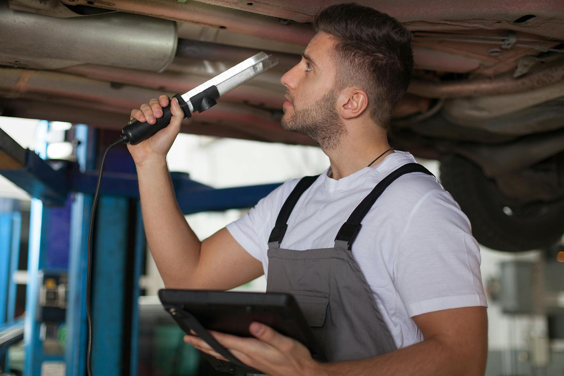 A mechanic inspecting the underbody of a vehicle with a light