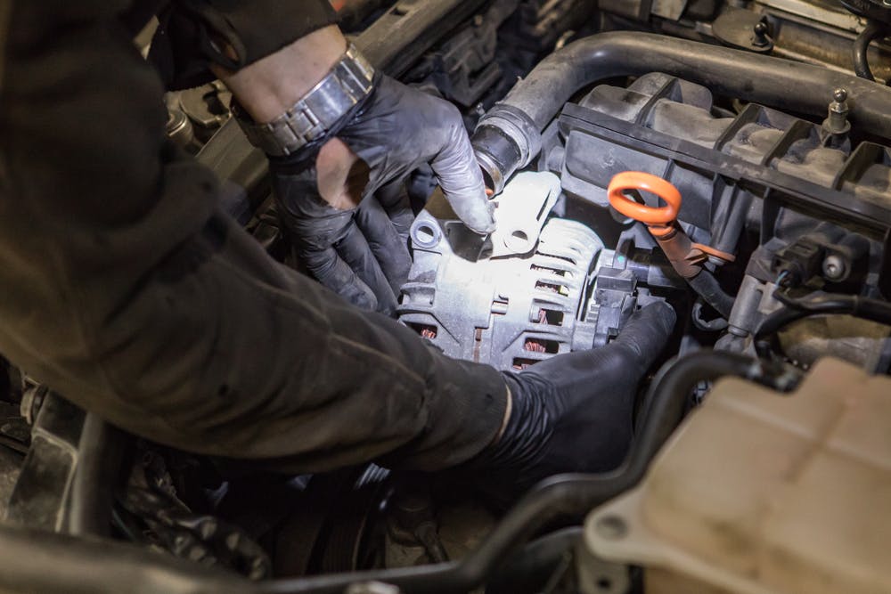 A man wearing gloves fitting an alternator to a car engine