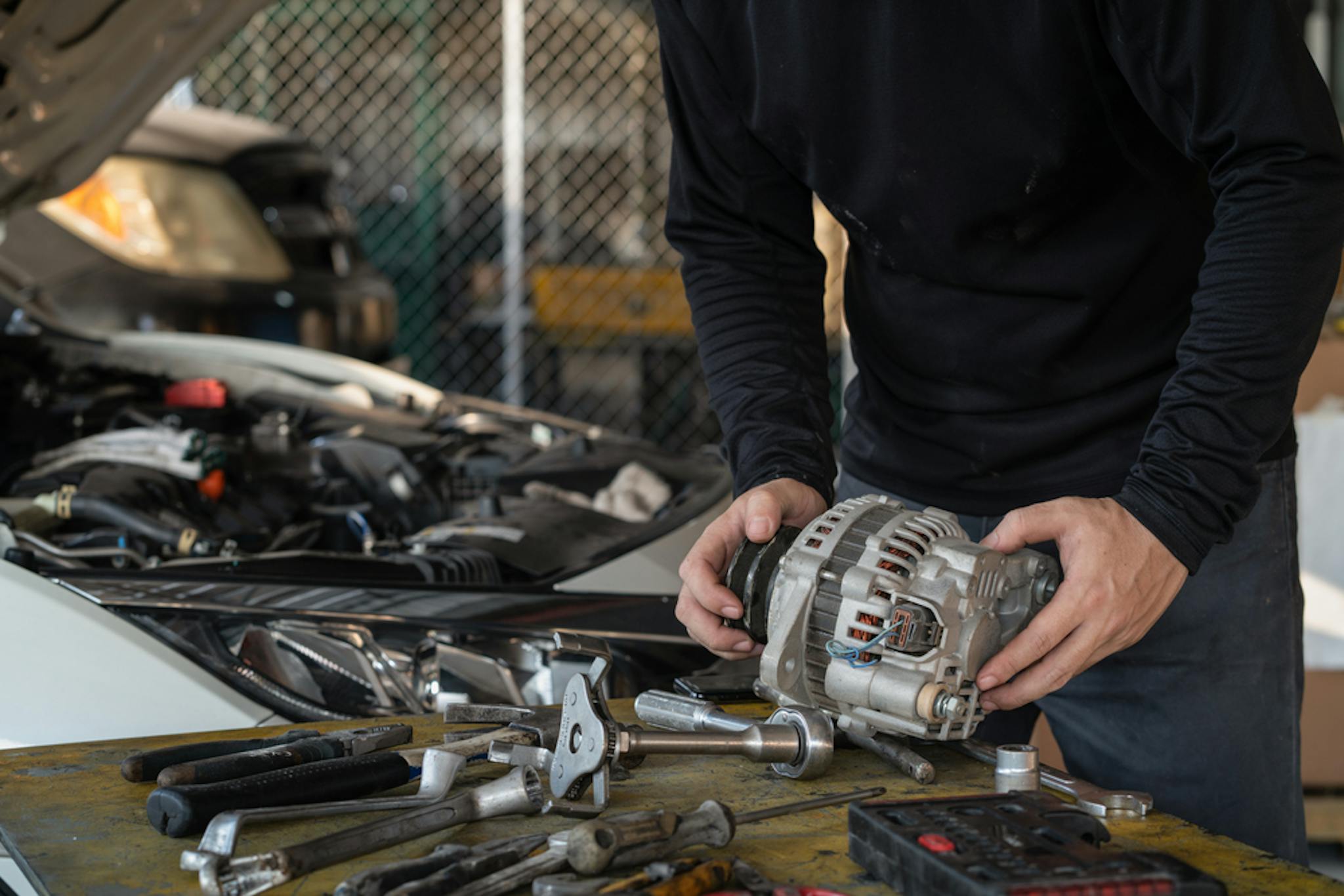 A man holding an alternator getting ready to fit it to a car