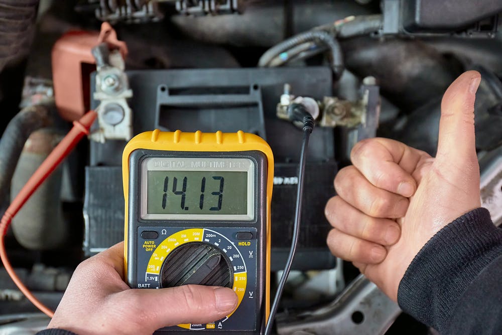 A person using a multimeter connected to a car battery to check the alternator performance