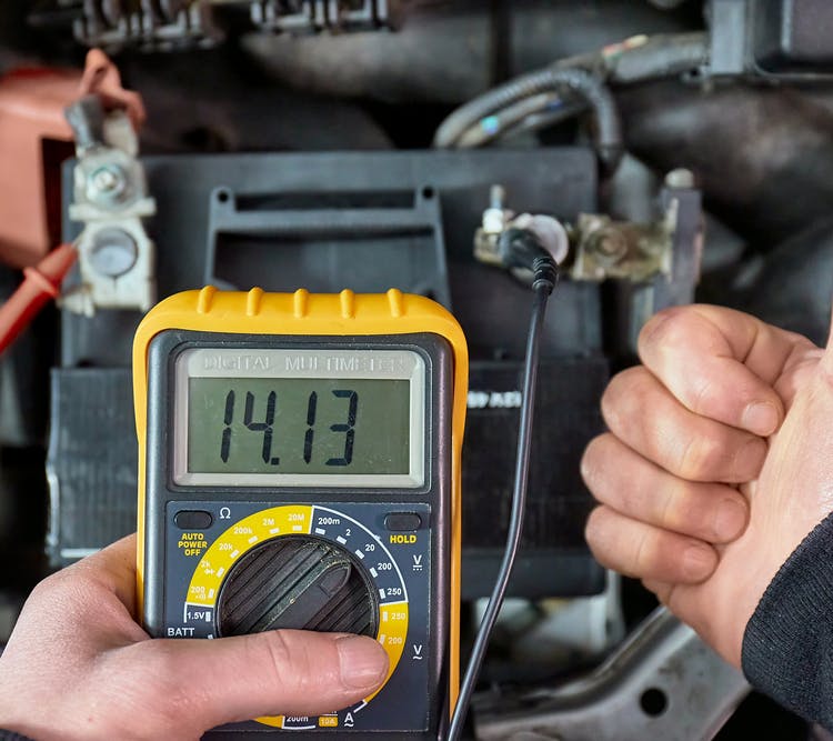 A person using a multimeter connected to a car battery to check the alternator performance