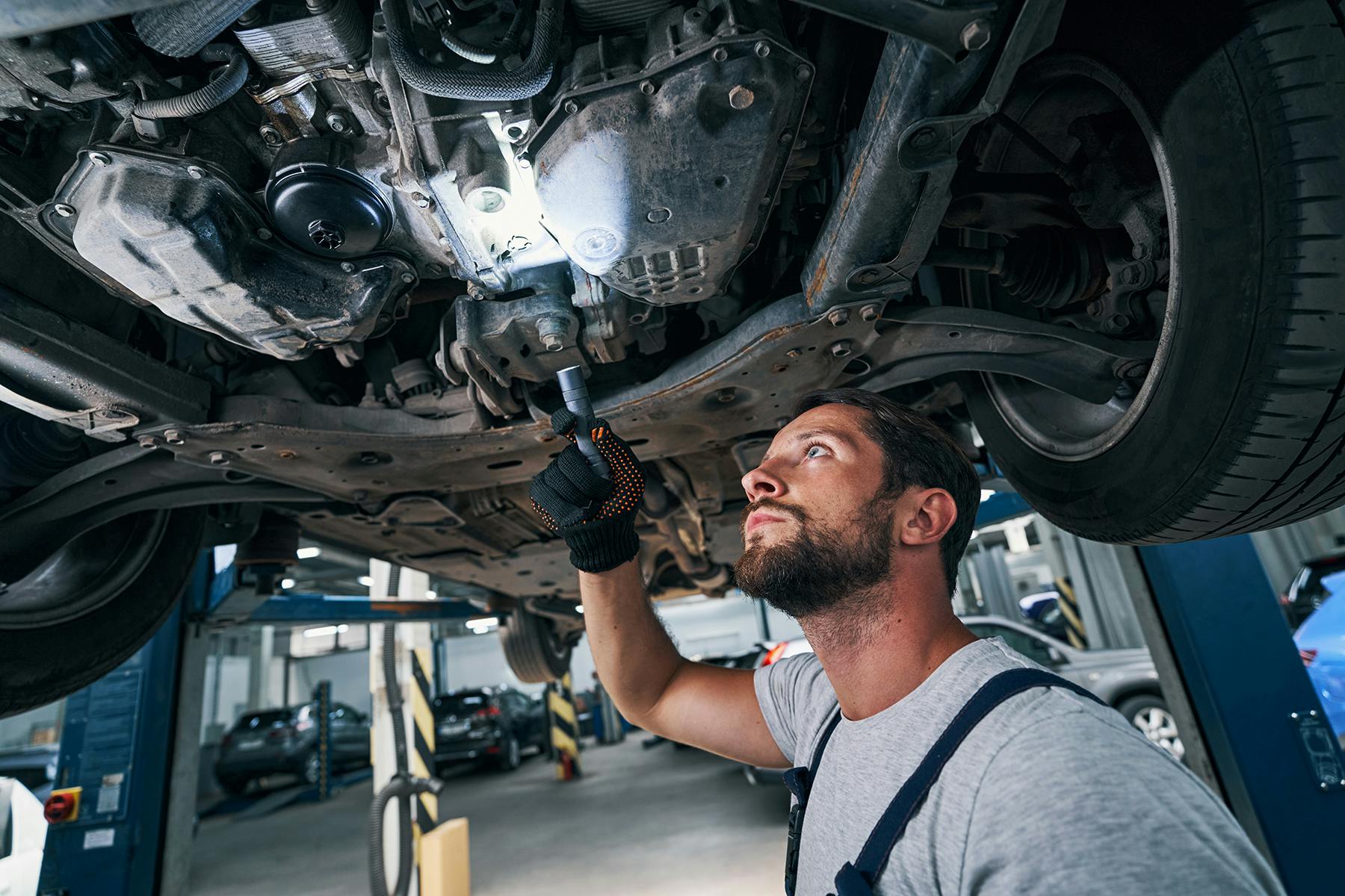 A mechanic inspecting the underbody of a car with a light