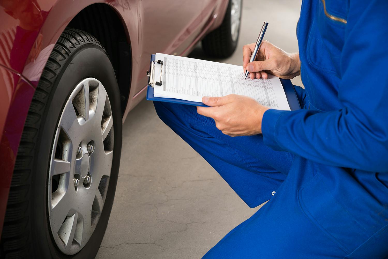 A mechanic inspecting a car wheel and filling out a form on a clipboard