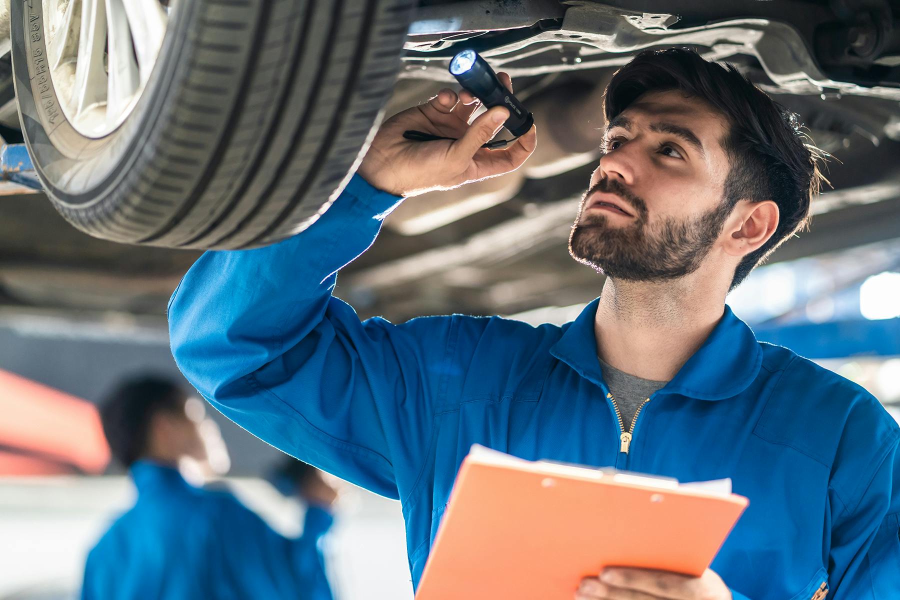 A mechanic inspecting the underbody of a vehicle with a clipboard