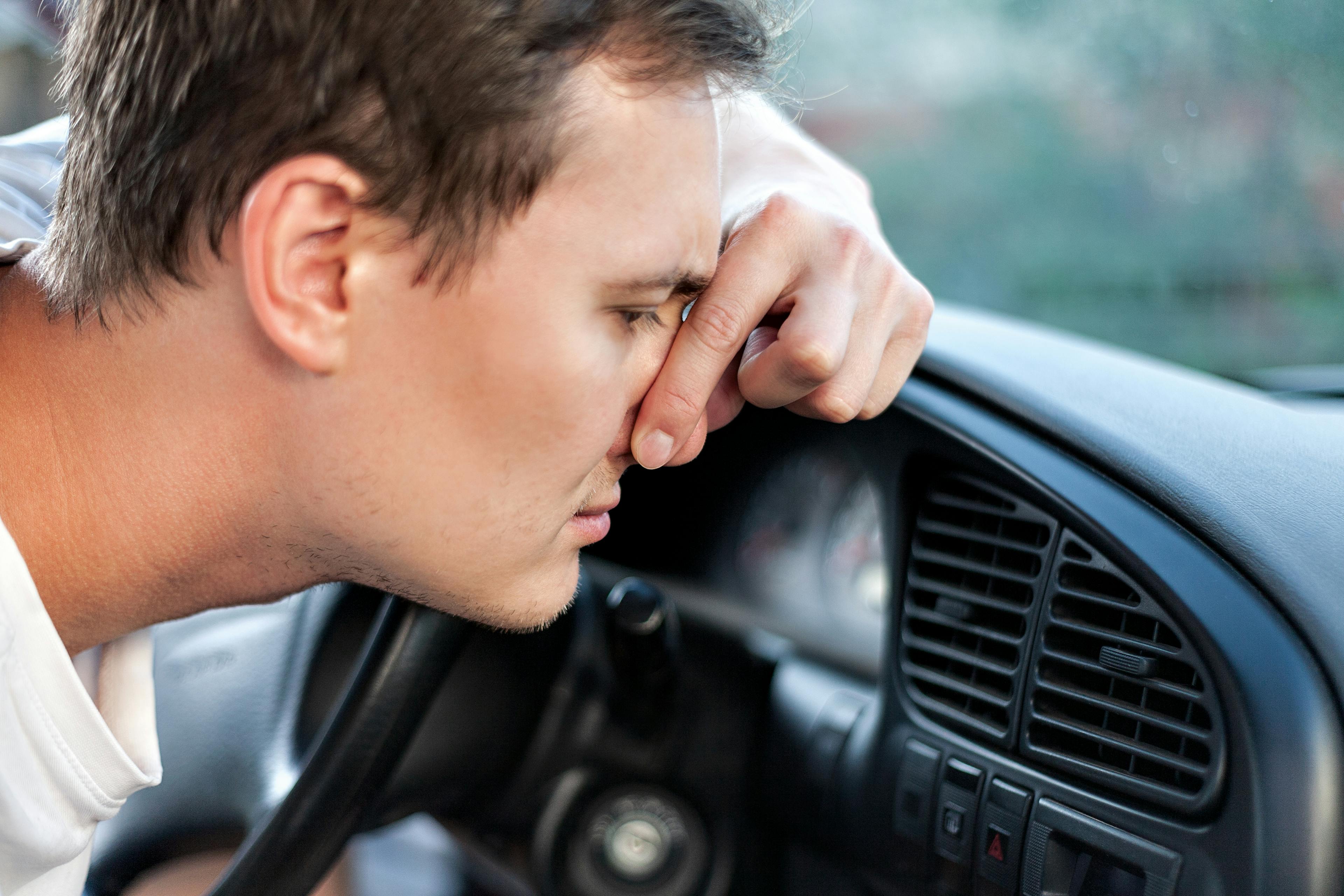 A man pinching his nose due to the smell of a car air conditioner vent