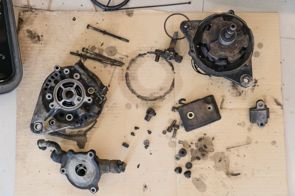 A dismantled car alternator on a cardboard sheet