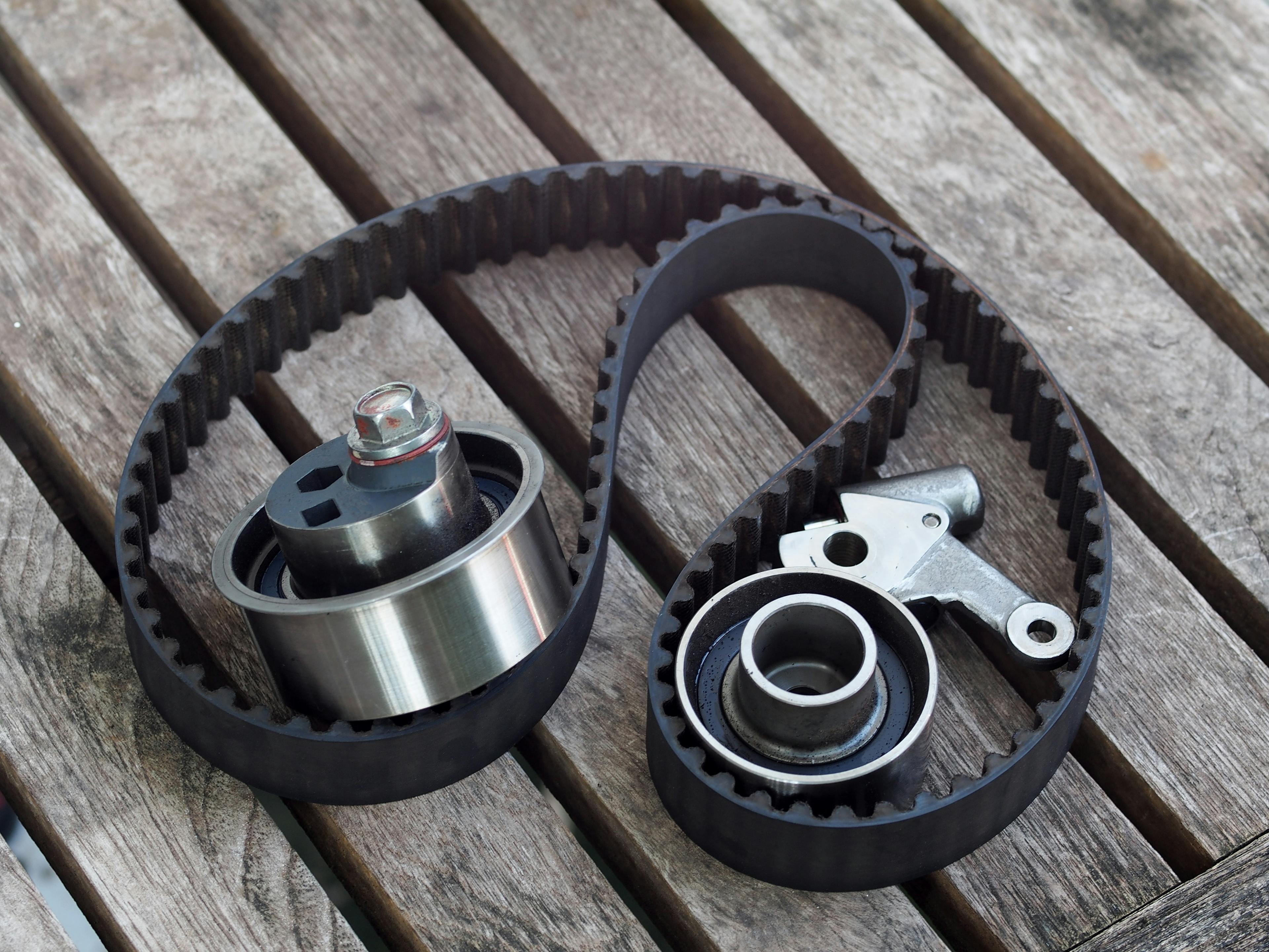 A timing belt, tensioner and idler pulley sitting on a wooden surface