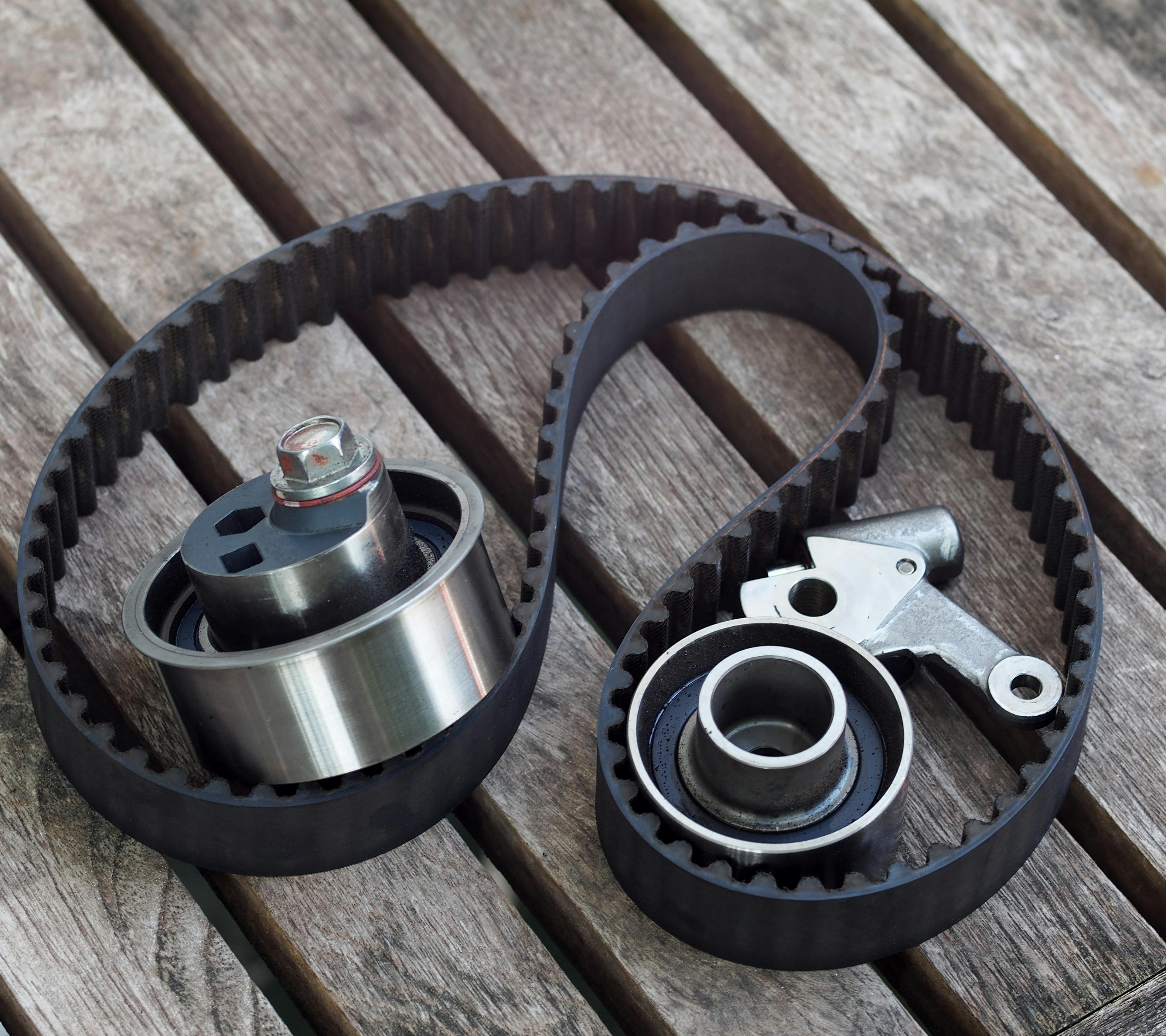 A timing belt, tensioner and idler pulley sitting on a wooden surface
