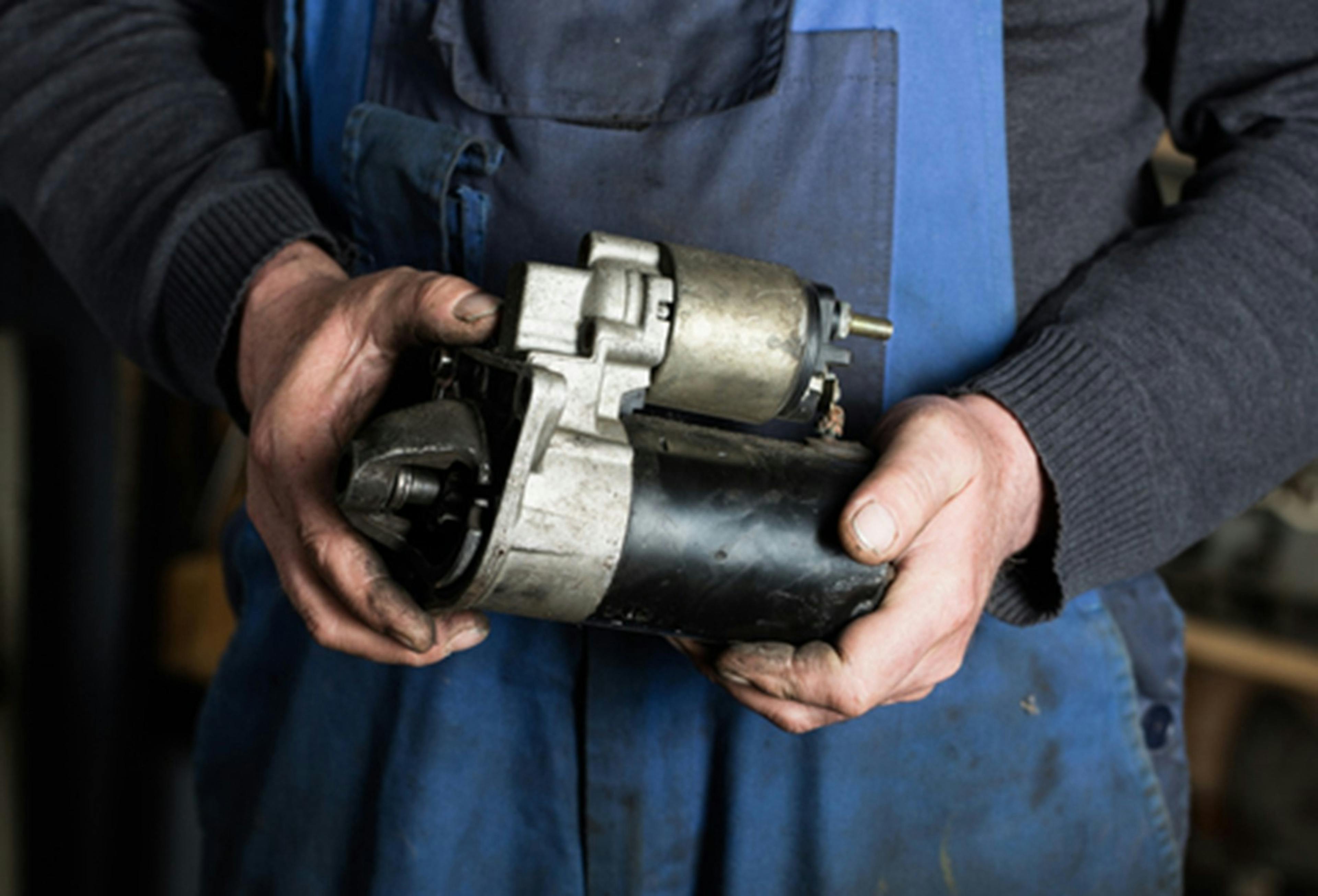 A mechanic holding a greasy starter motor