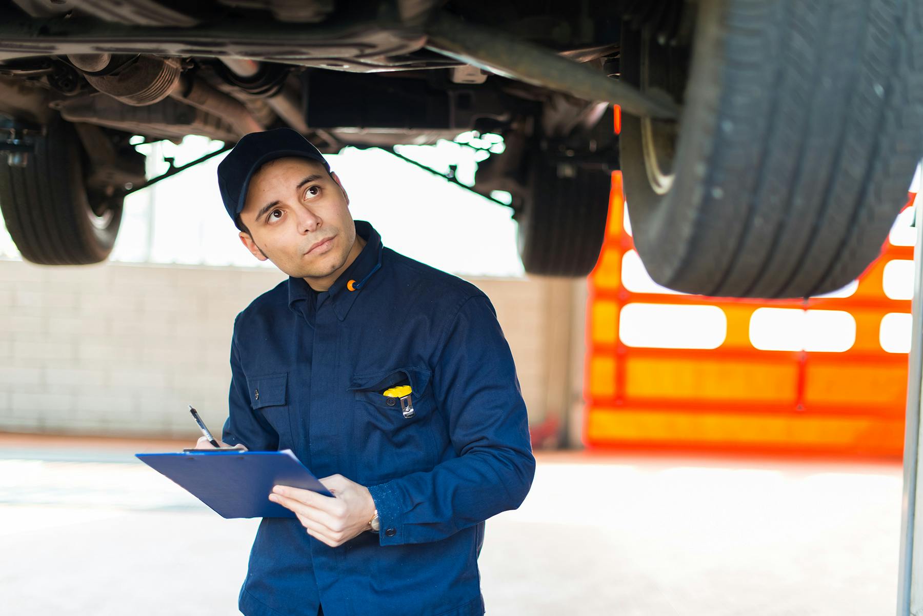 A mechanic with a clipboard inspecting the underbody of a car