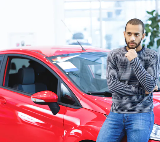 african american man contemplating while leaning against a red car