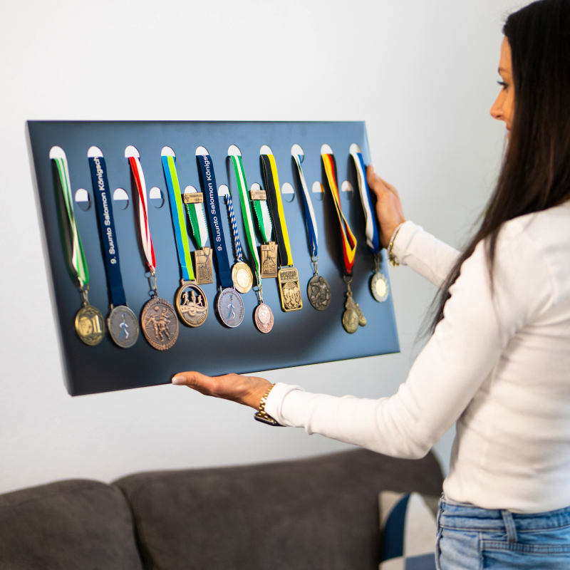 Frau zeigt Medaillenhalter aus Aluminium mit aufgehängten Medaillen im Wohnraum