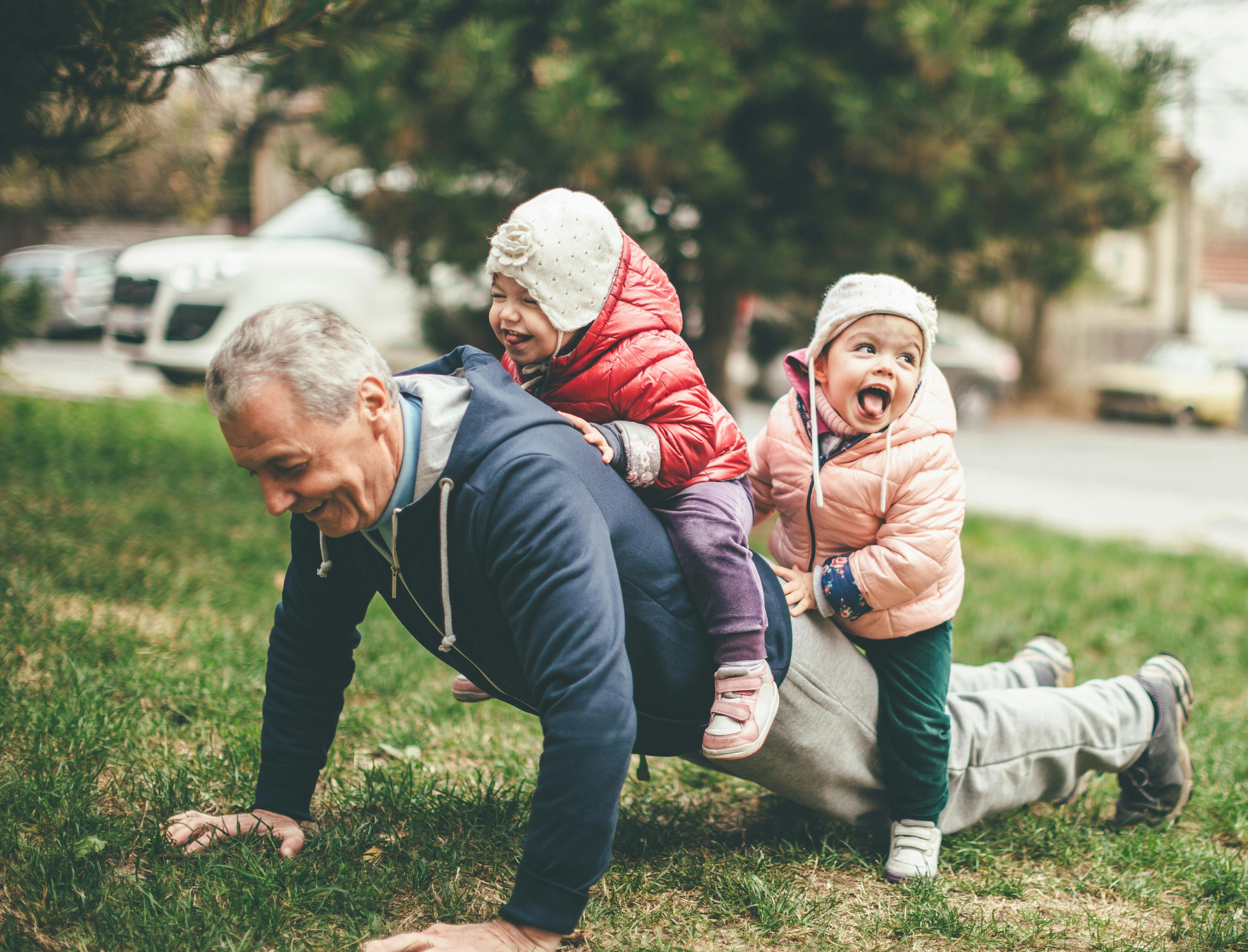 An older man doing push ups with small children on his back