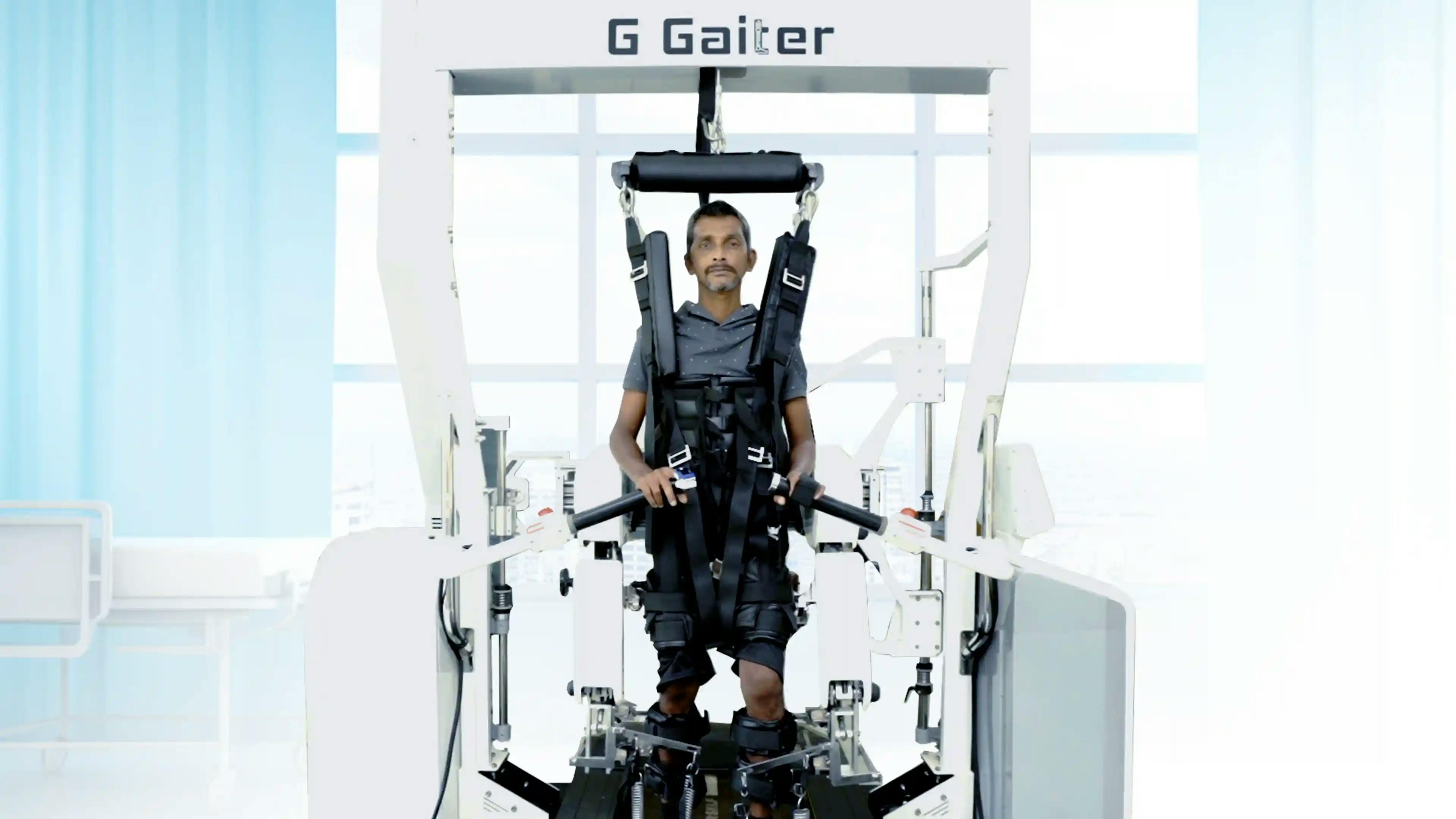 Patient undergoing robotic-assisted gait training on the G Gaiter system at General Hospital Thiruvananthapuram, supported by suspension harness and guided lower-limb movement.