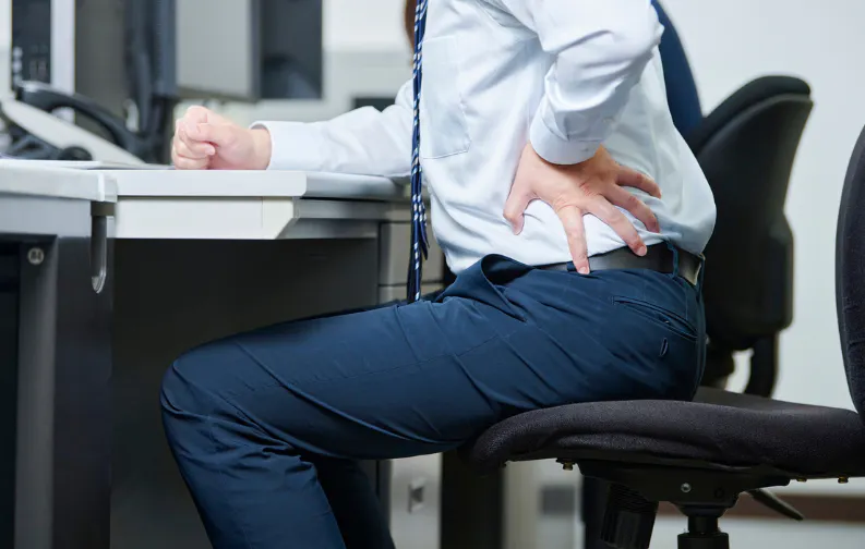 Mann im Büro fasst sich an den Rücken