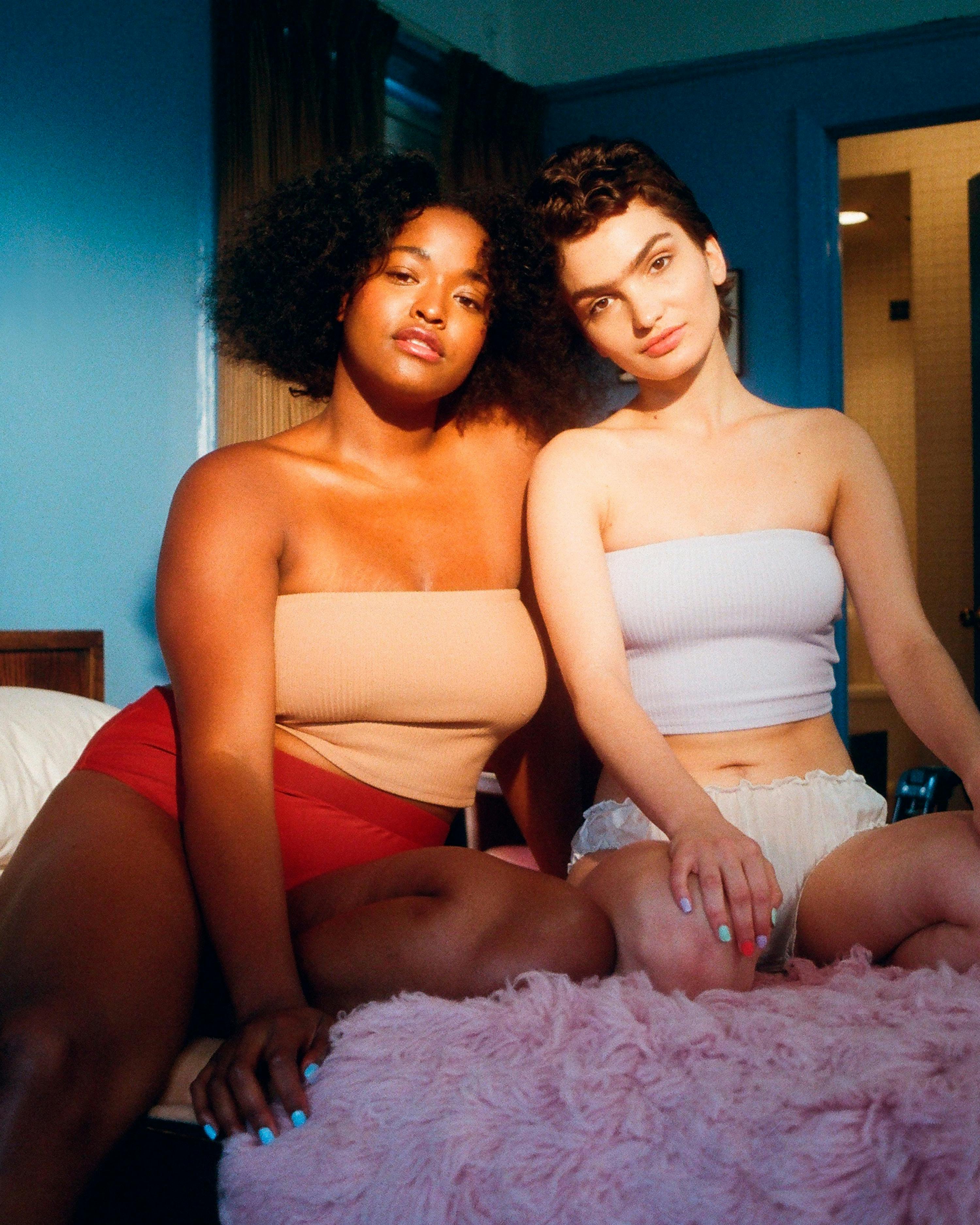 Photo of two body positive women sitting in bed.