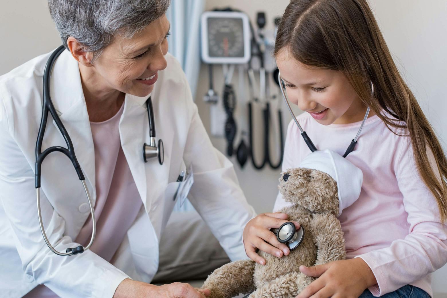 A photo of a pediatric physician examining a patient, who is holding a teddy bear, in relation to the Affordable Health Care Act.