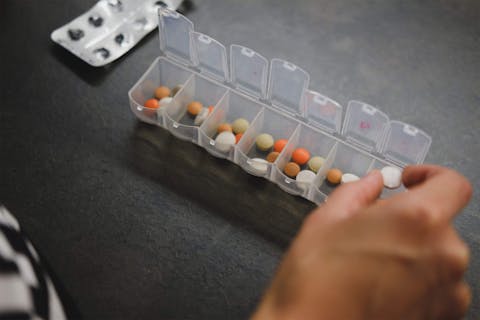 A photo of a woman's hand as she hovers over a pill container thinking about which alternative to Zantac she should select. 