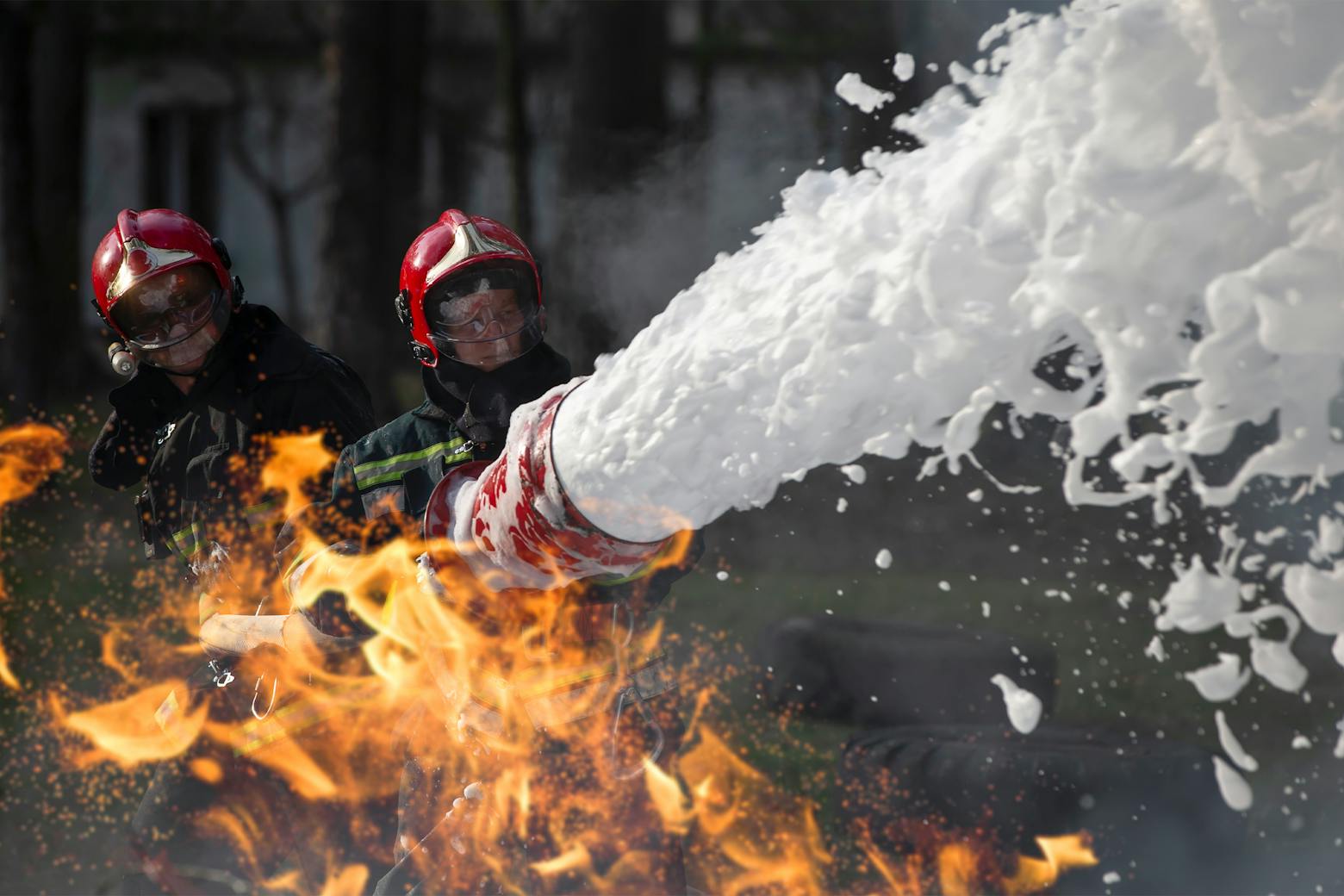 Two firefighters using aqueous film-forming foam to fight a fire, representing the PFAS class action.