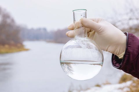 A photo of a researcher holding a beaker of water, representing PFAS, the toxic chemical that is found in drinking water.