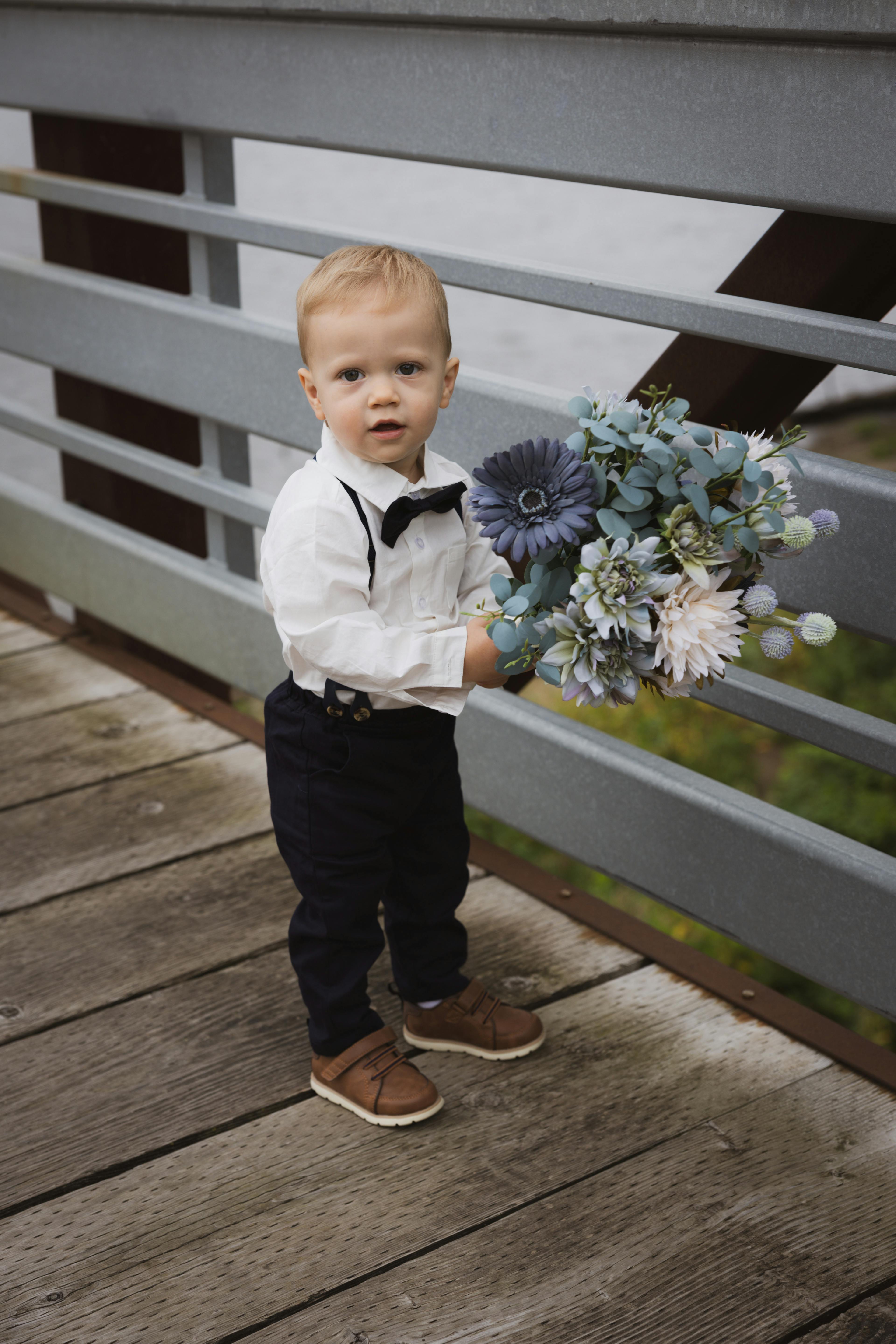 child in a formal suit holding flowers on a bridge