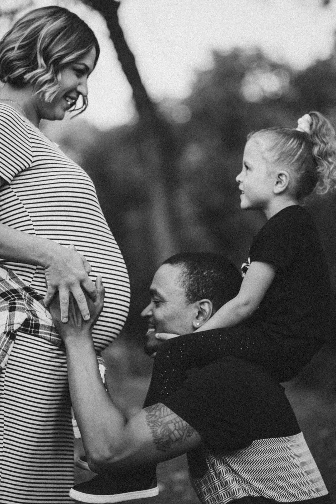 father kissing pregnant belly and while first born is sitting on dad's shoulders