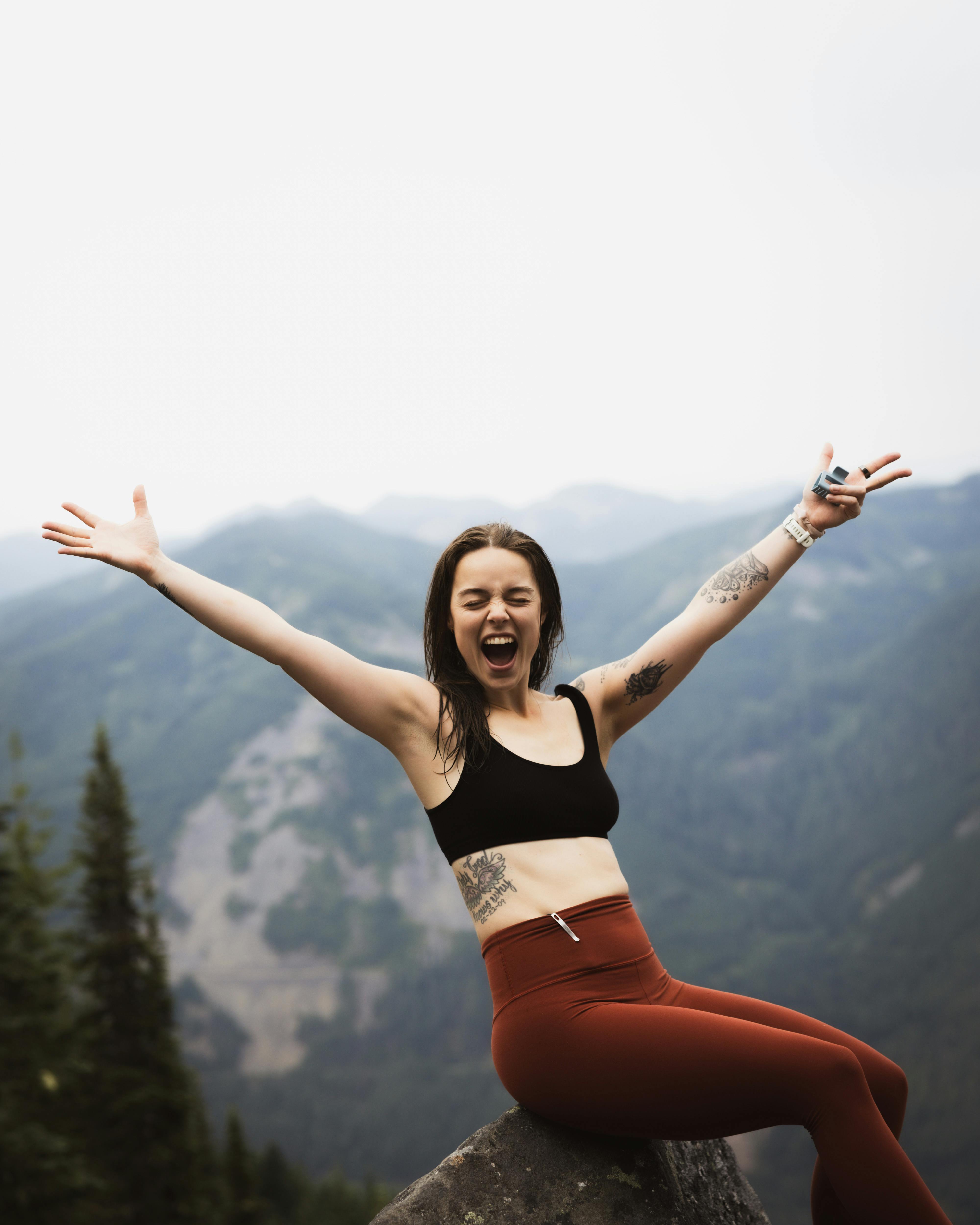 woman on top of a mountain with her arms up to the sky scream of joy