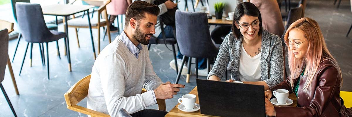sales meeting in a coffee shop with three diverse people looking at a laptop