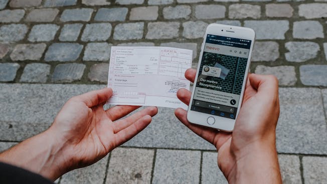 Mann hält Handy und Rezept in der Hand.