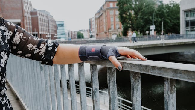 Frau trägt Bandage und greift ein Geländer.