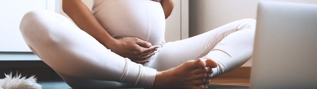 Frau sitz schwanger und im Schneidersitz auf Yogamatte