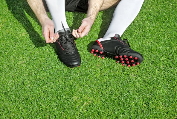 Mann schnürt Fussballschuh auf Rasen