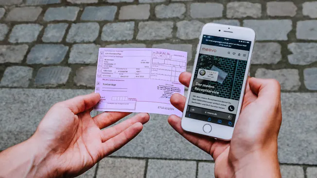 Mann hält Rezept und Handy in der Hand.