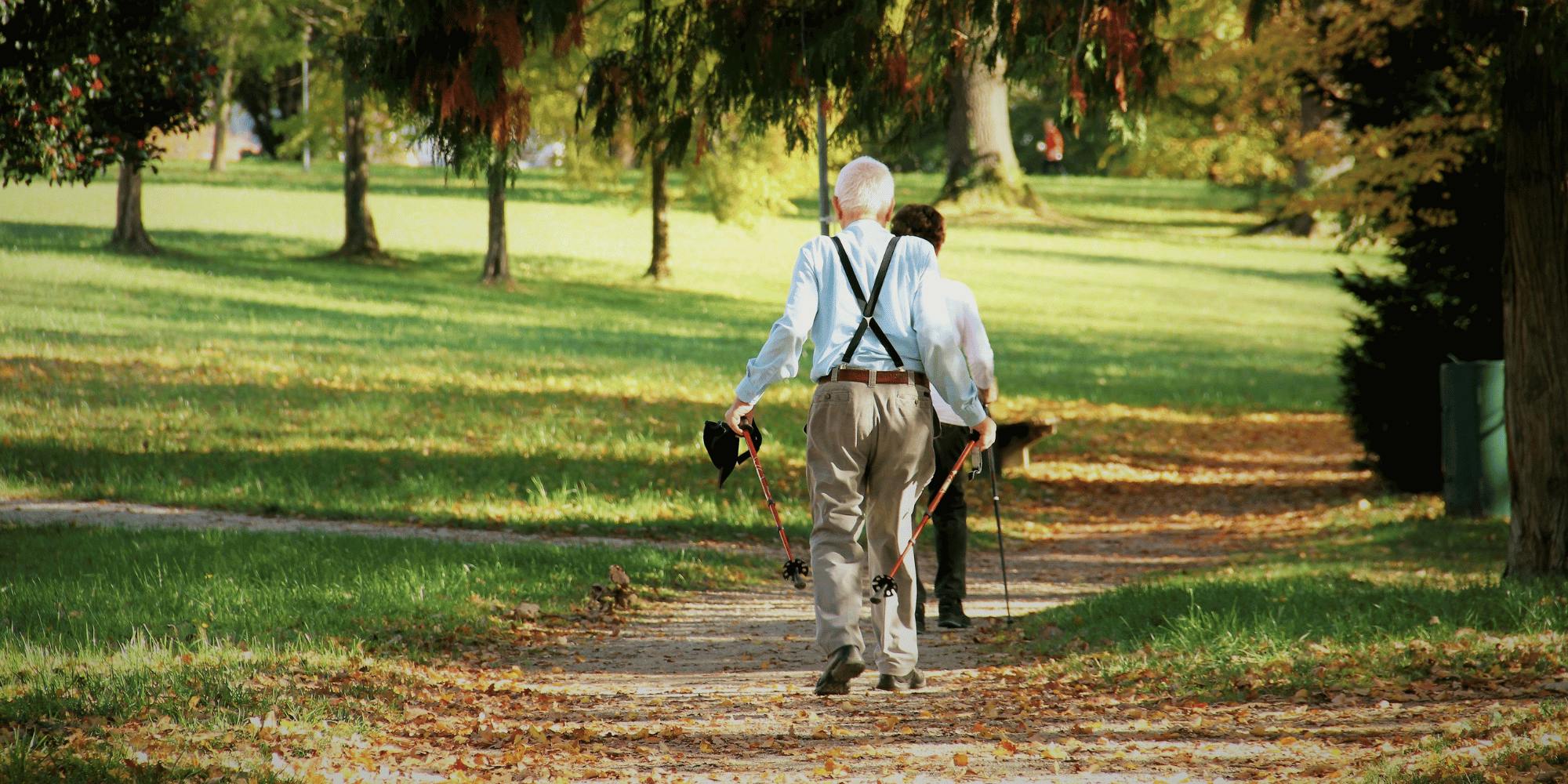 Seniorenpaar läuft mit Walking-Stöcken durch den Park. 