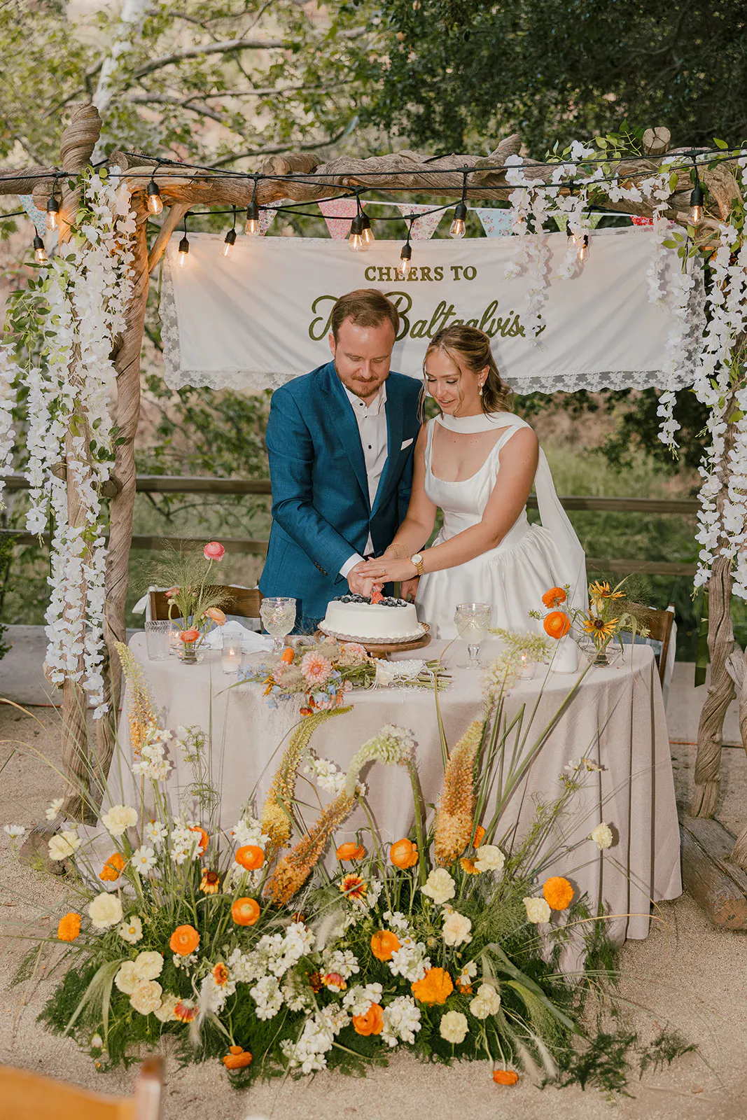 cutting  the cake with wildflowers and lacey camp inspired wedding welcome signs